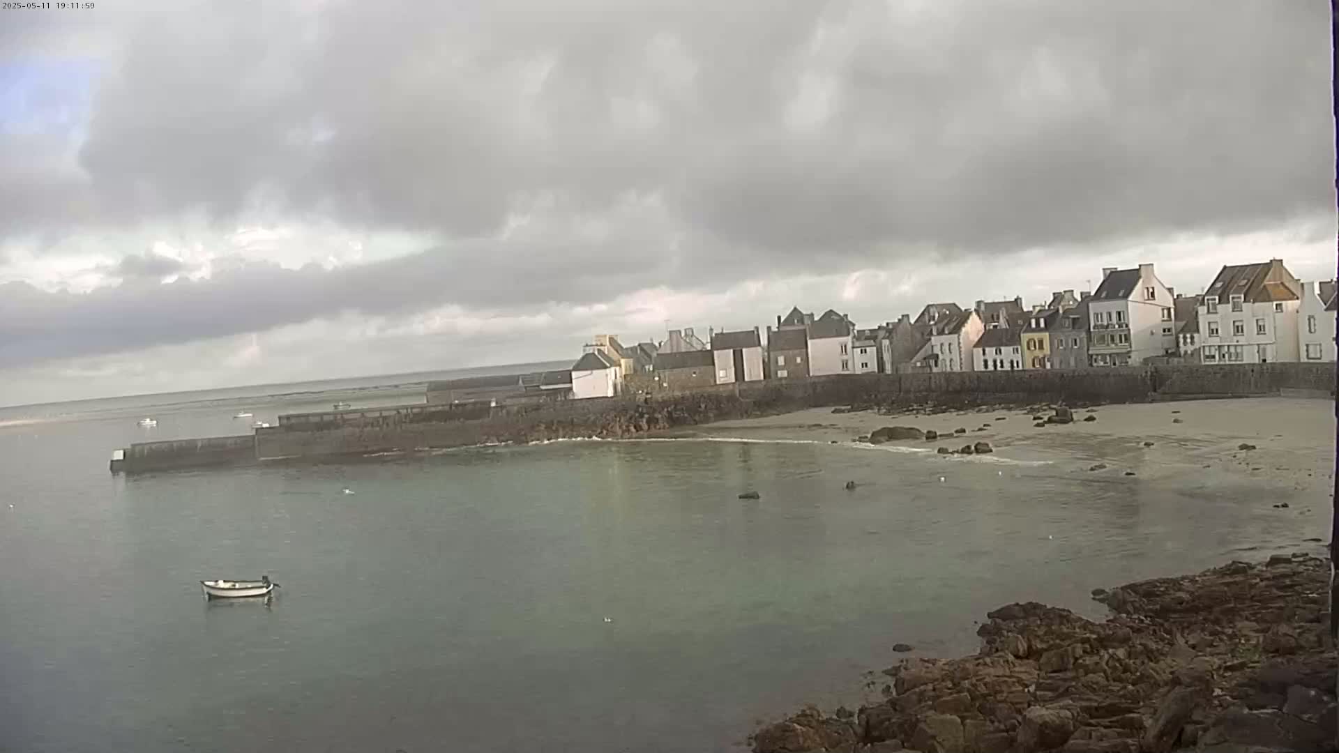 A small, calm harbor with a row of buildings along the shore under an overcast sky.