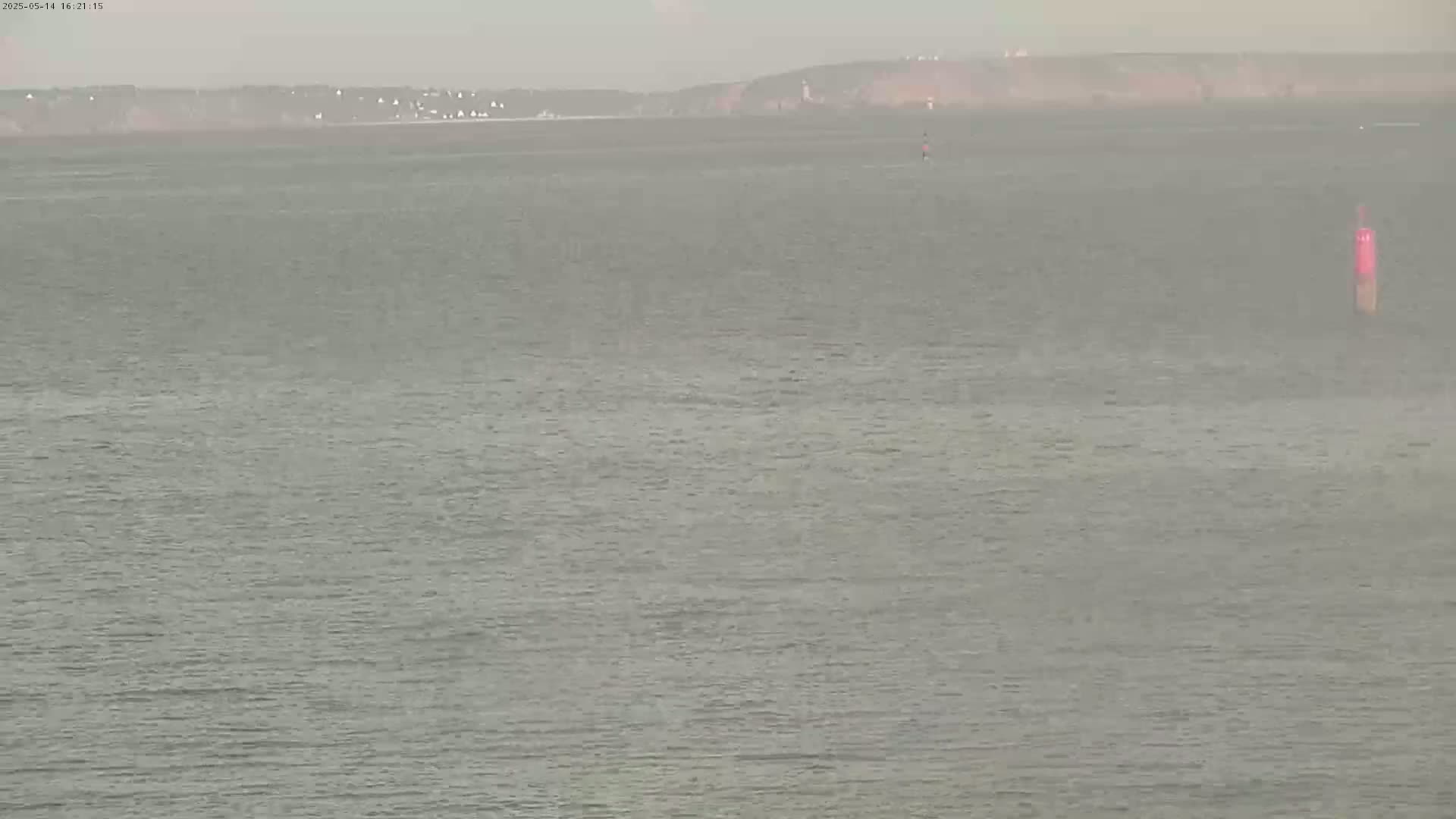 A hazy, overcast day reveals a calm body of water with a distant shoreline and a single marker buoy.