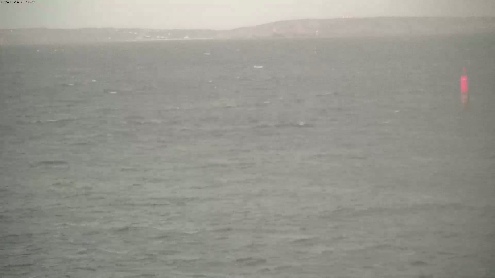 A choppy sea is visible under an overcast sky, with a distant shoreline barely discernible in the mist.