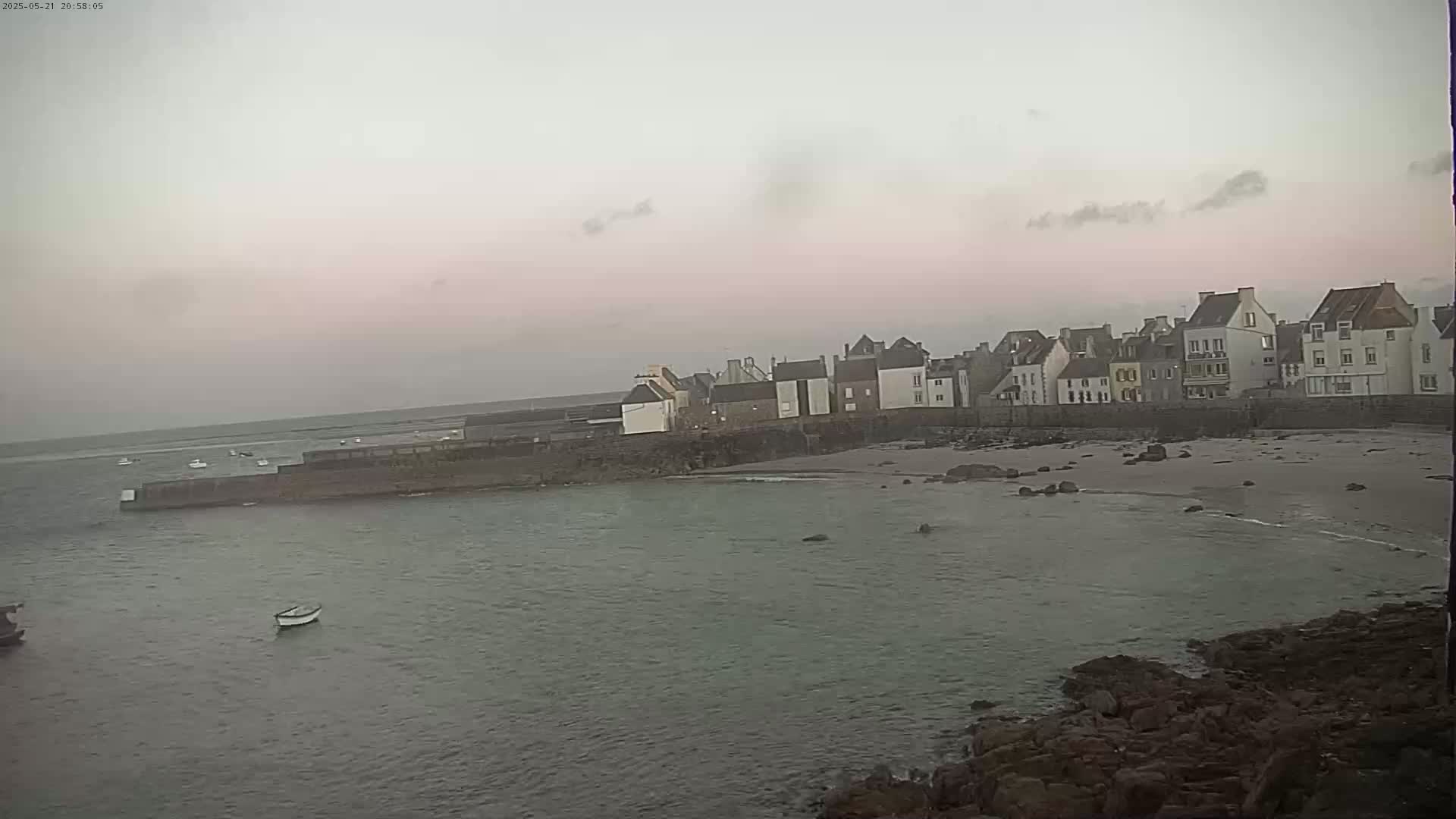 A row of buildings lines a calm body of water under a pale pink and gray sky.