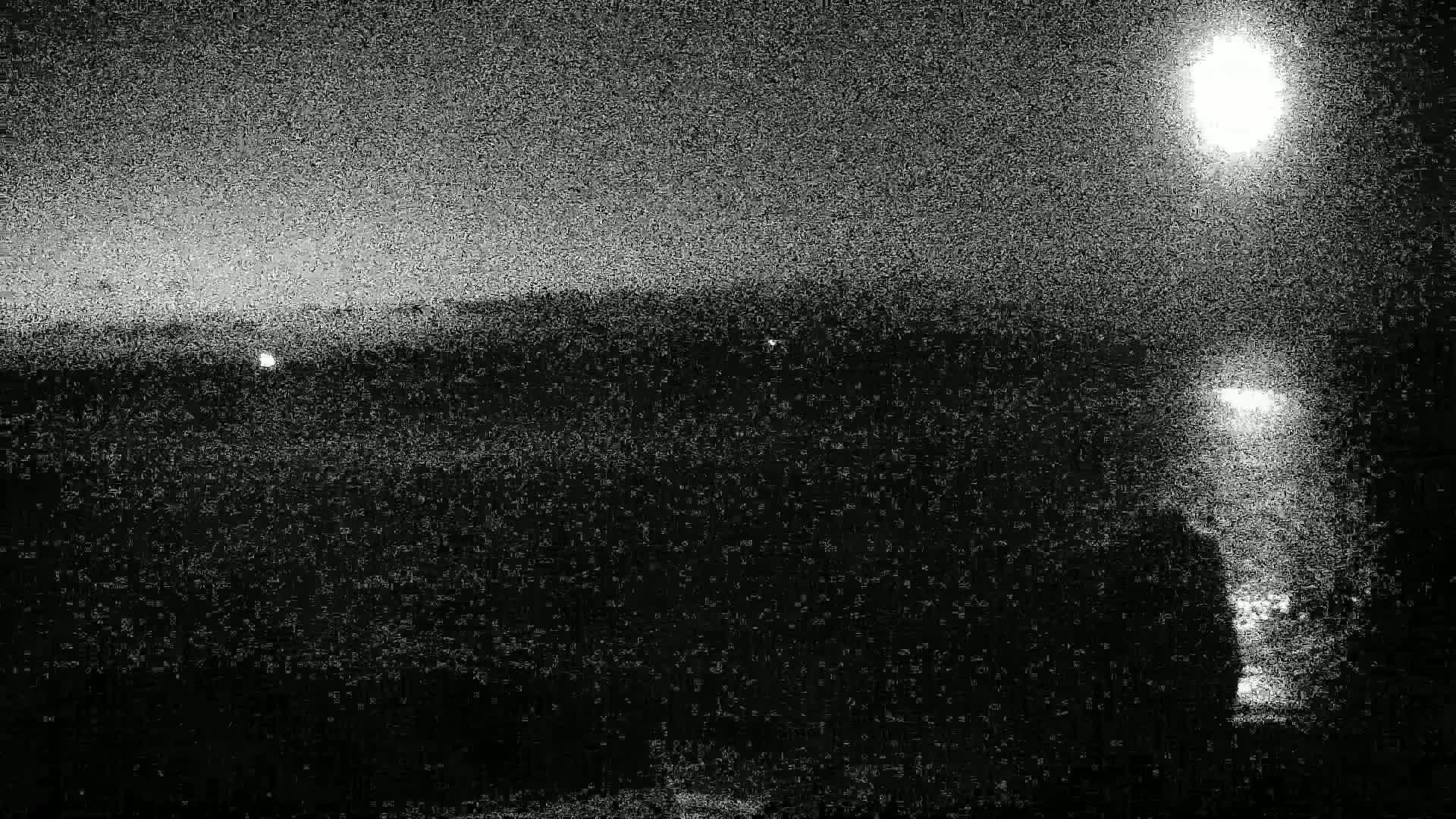 A nighttime, grainy image shows a dark landscape under a bright moon and several distant lights.