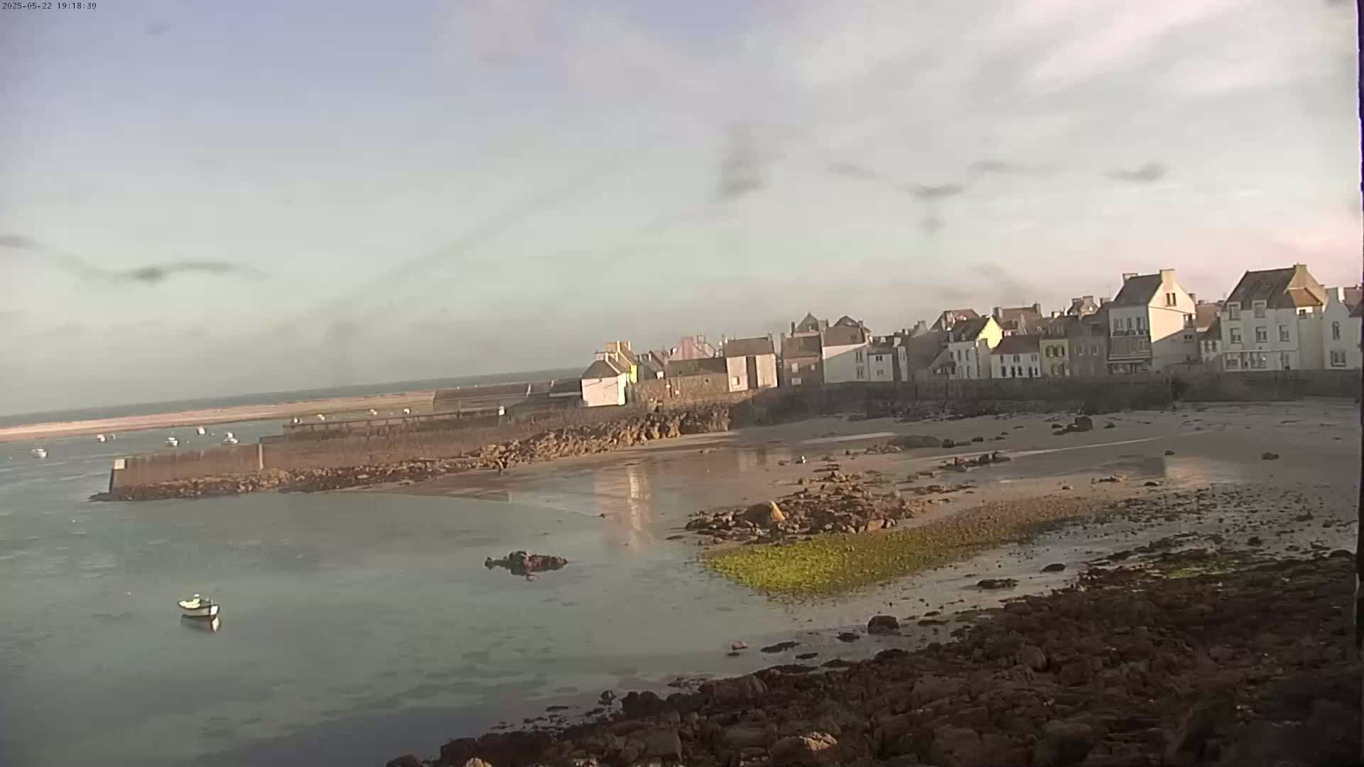 A small coastal town with a sandy beach and calm water is seen under a cloudy sky.