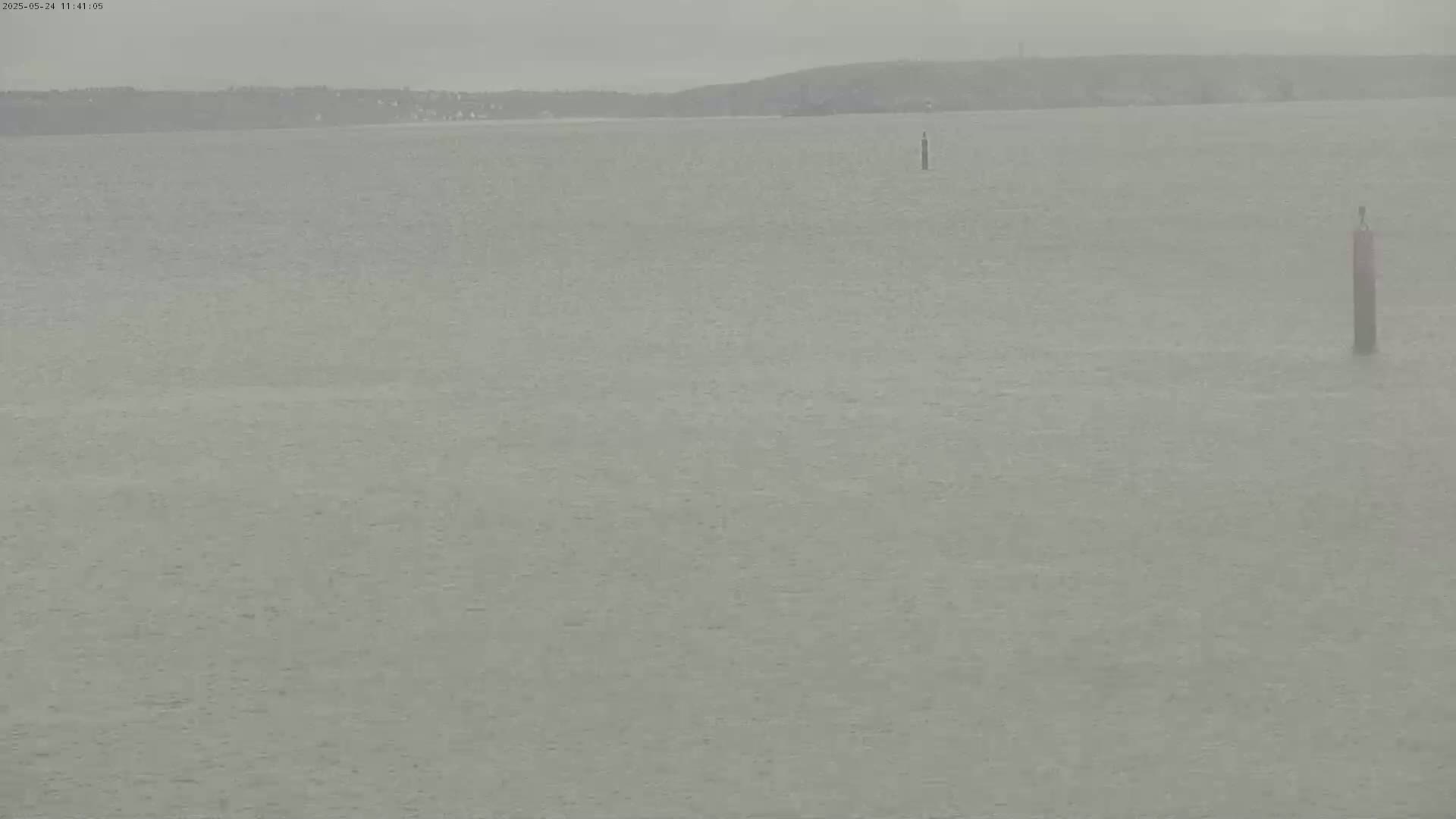 A calm body of water stretches to a hazy shoreline under an overcast sky.