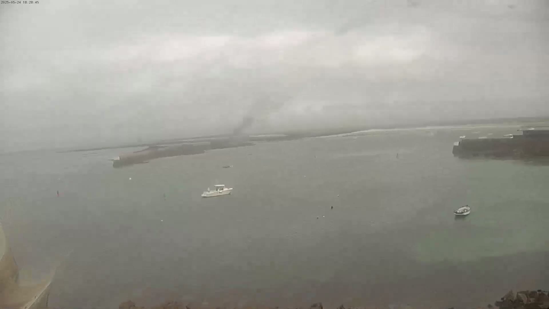 A hazy, overcast day shows a calm body of water with a few small boats and distant landmasses.
