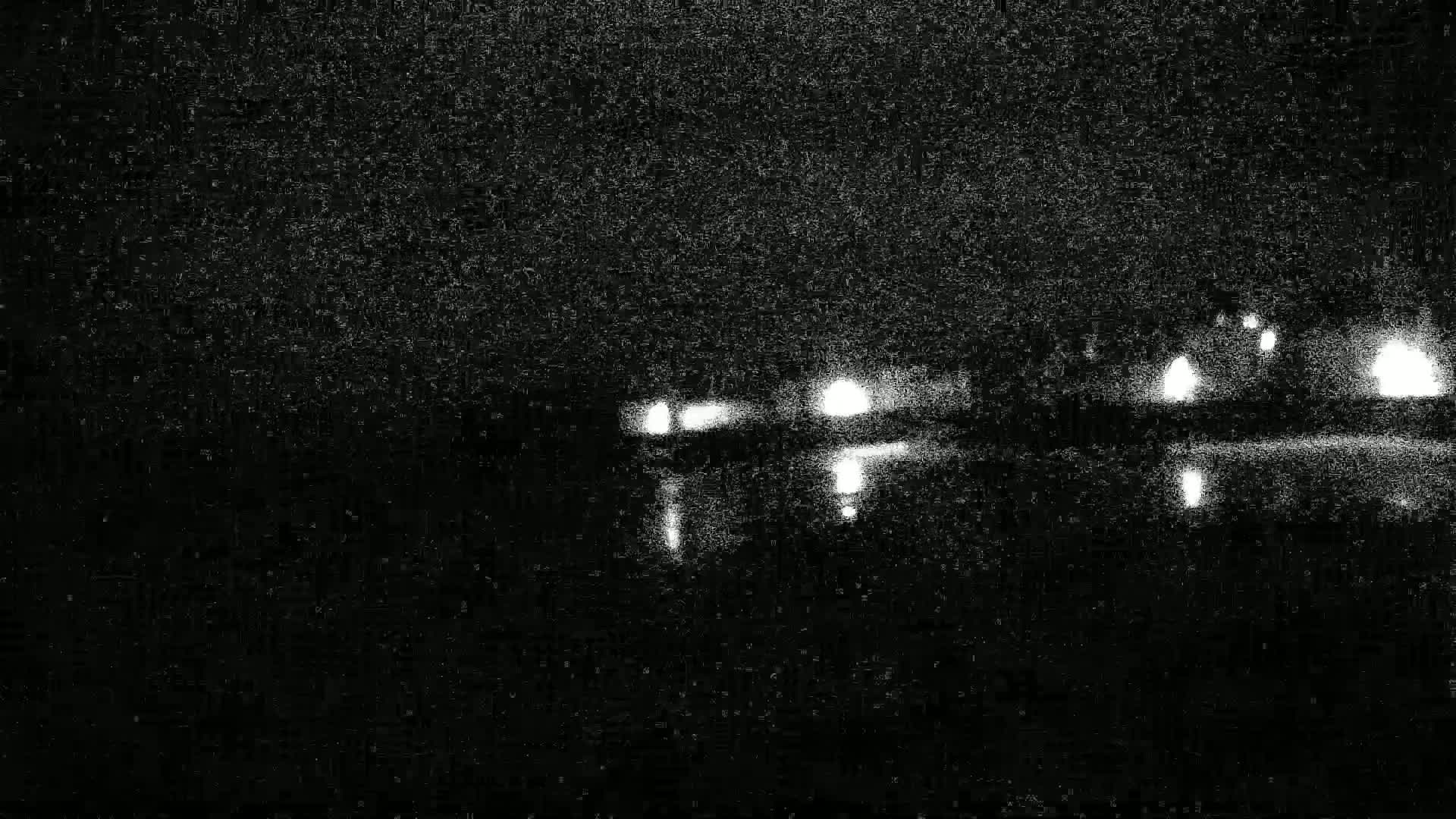 A blurry, nighttime image shows a distant line of lights, possibly from buildings or vehicles, under a dark, grainy sky.