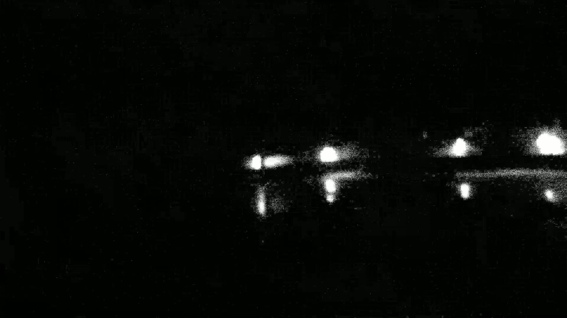 A blurry image shows the faint lights of several vehicles at night on a dark road.
