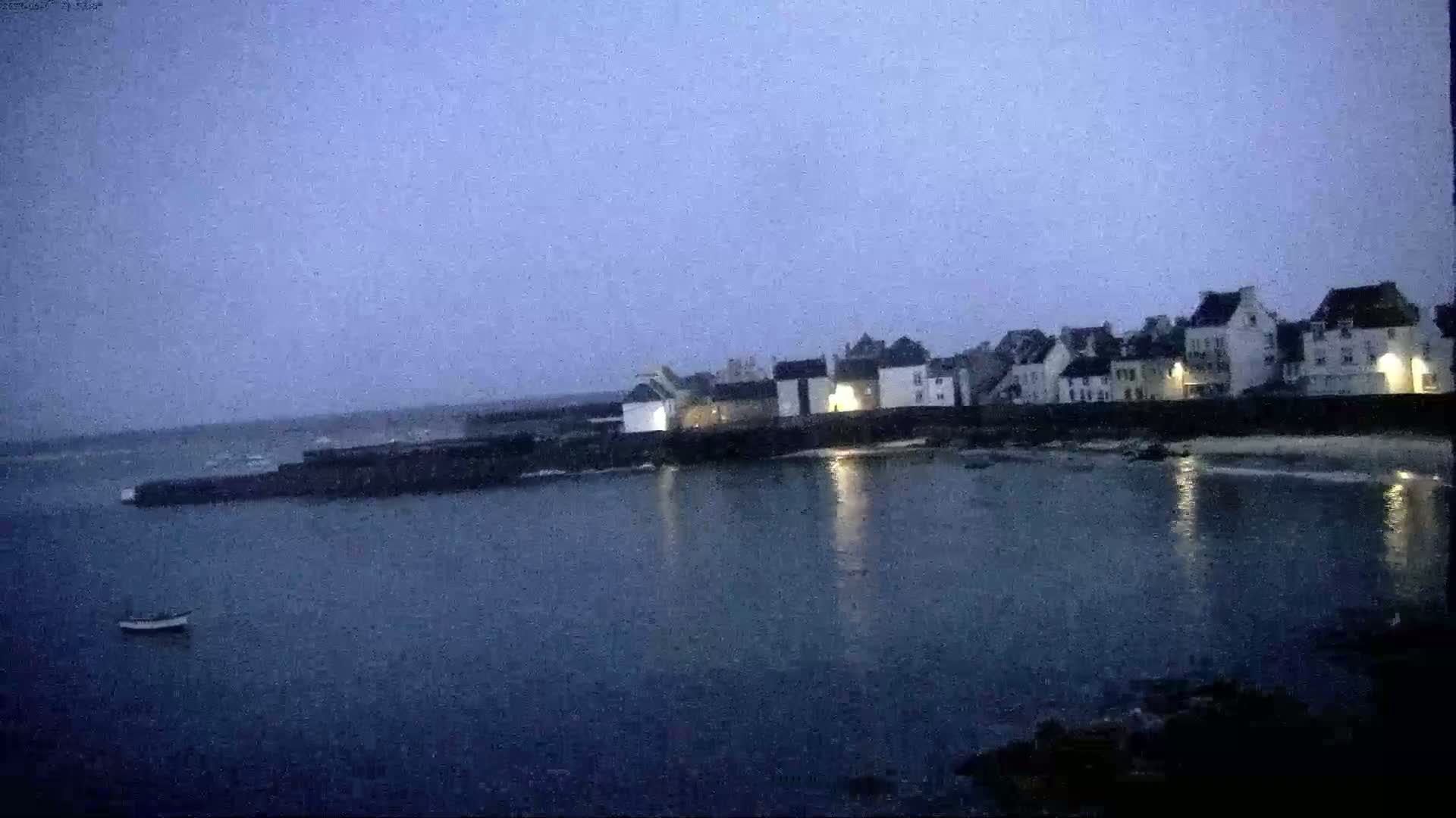 A small, quiet village sits on a dark, calm body of water under a twilight sky.