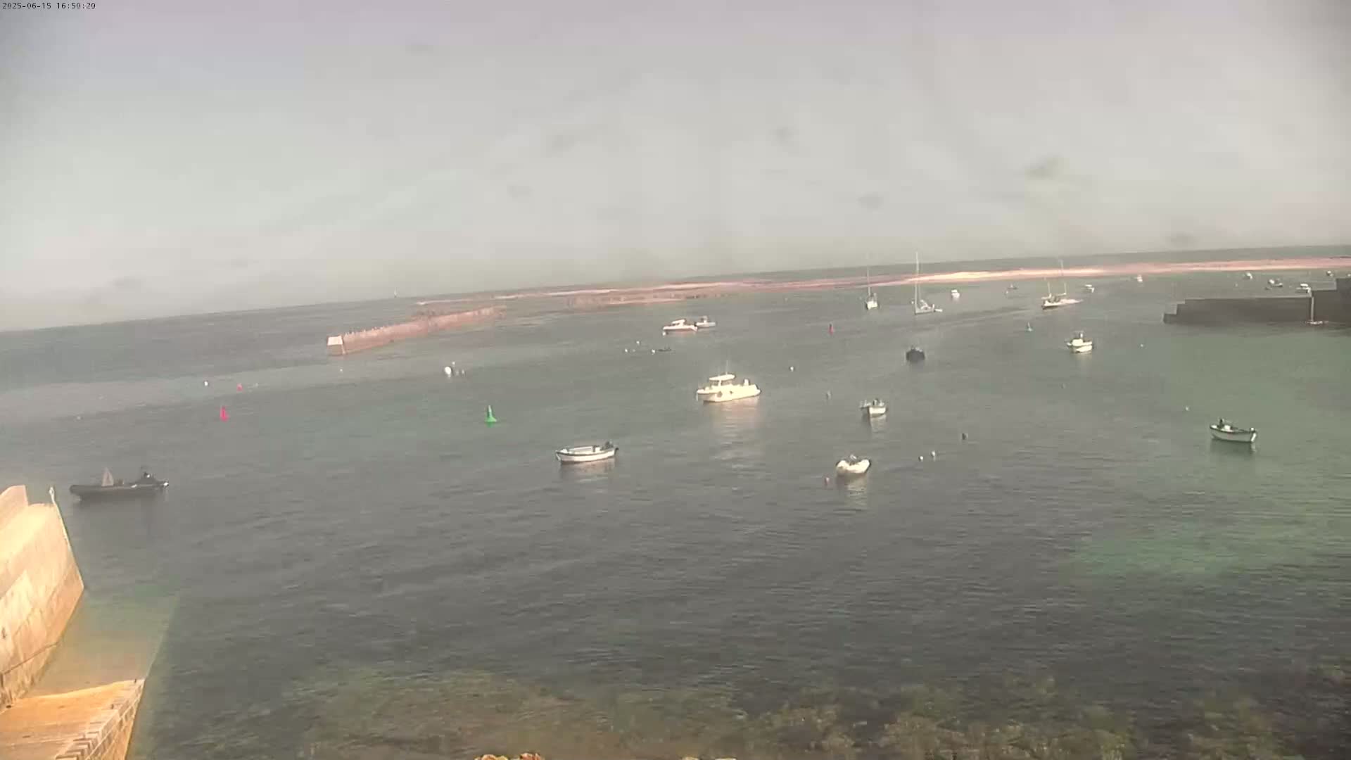 Several boats are moored in a calm harbor on an overcast day.