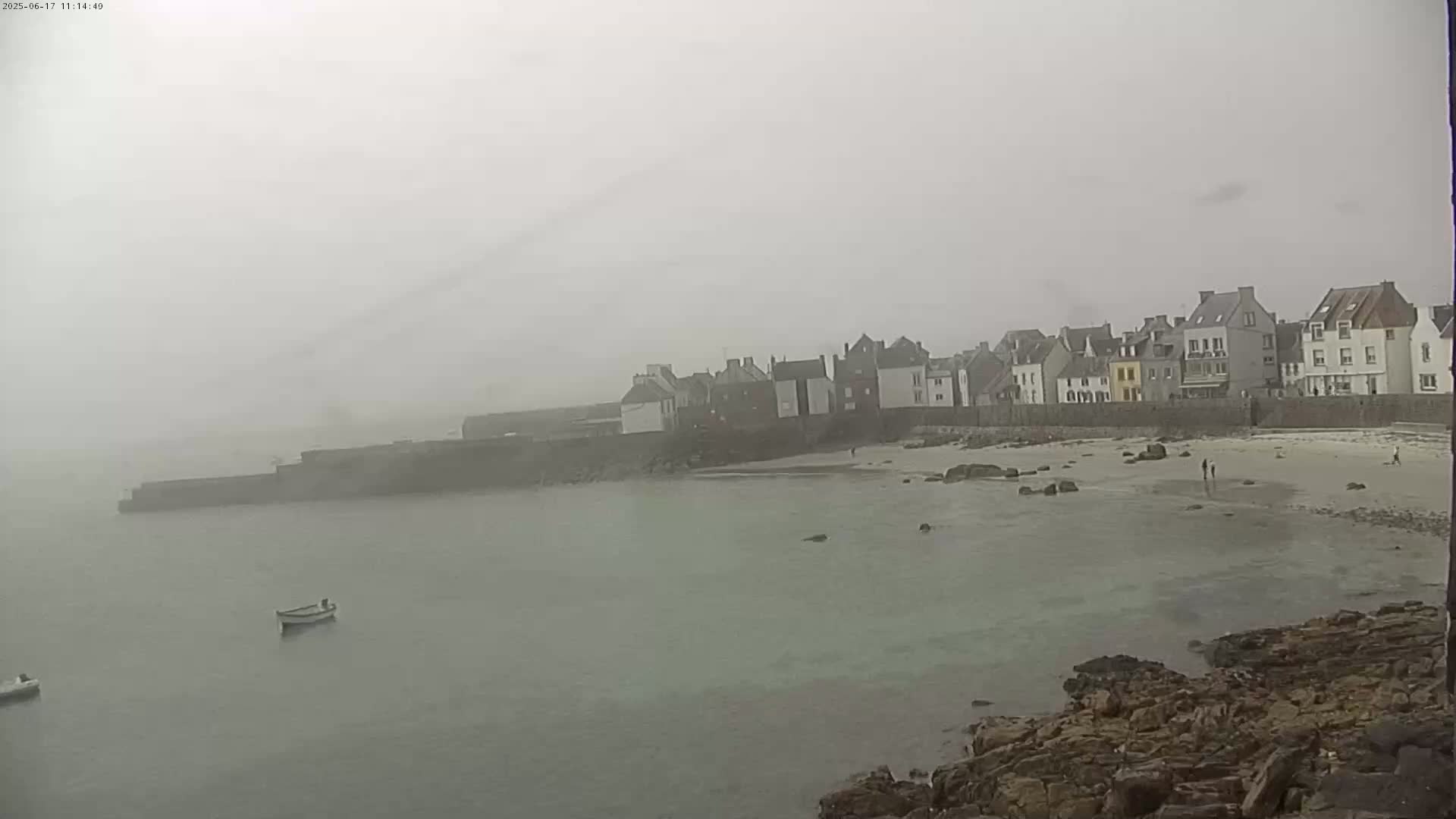 A foggy coastal town with a small sandy beach and a few boats in the water.