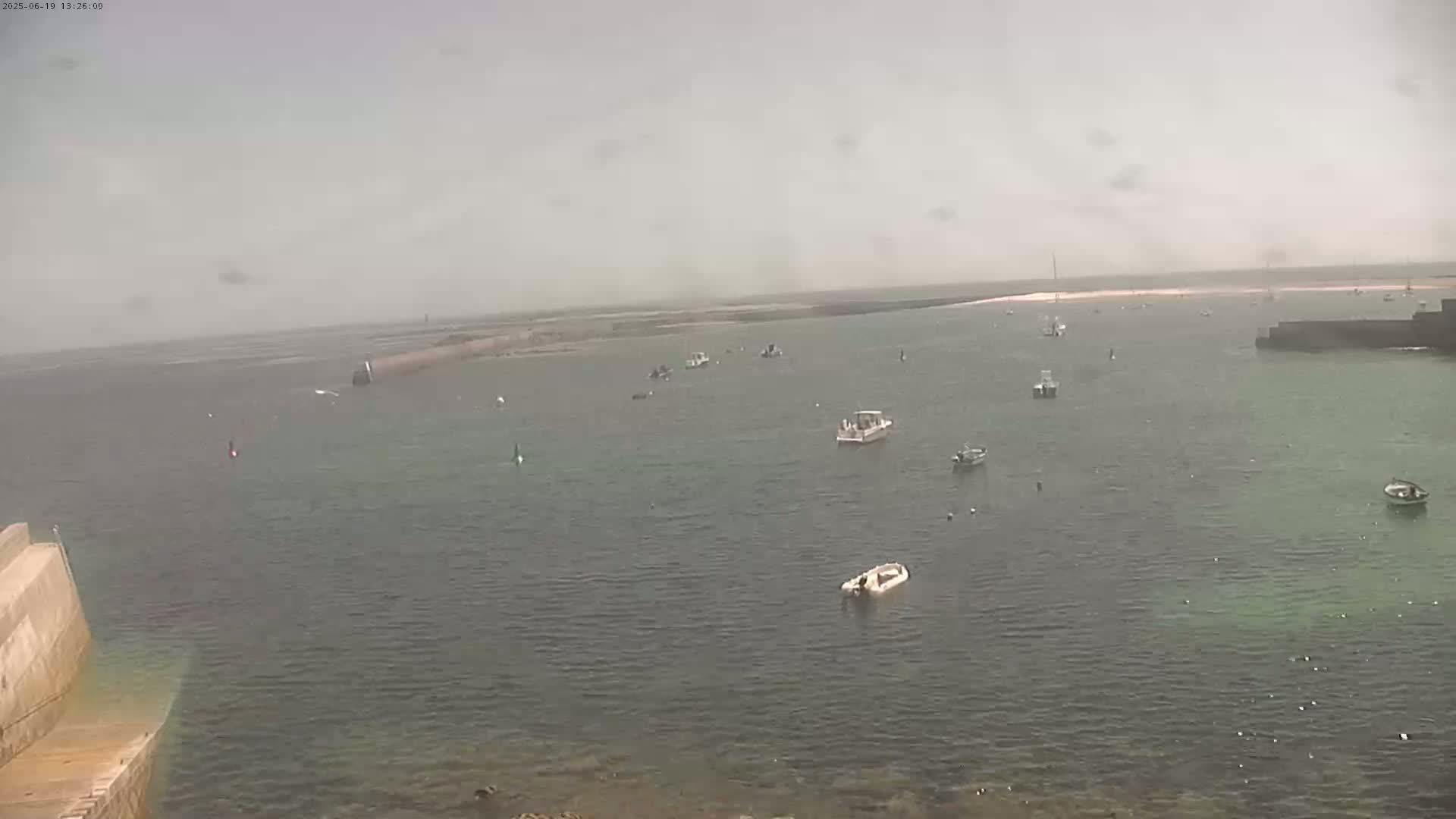 Several small boats are moored in a calm, hazy harbor.