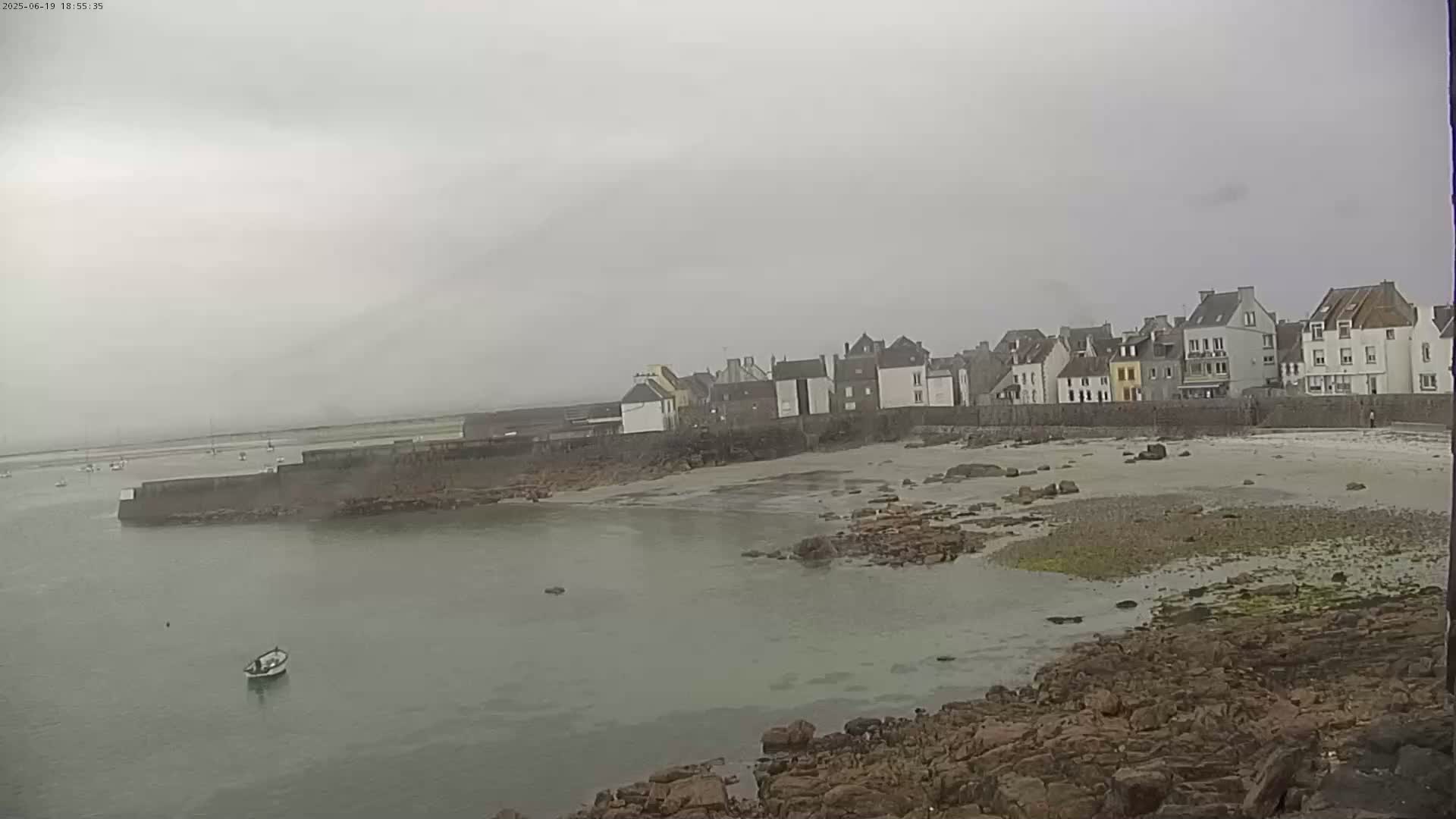 A small coastal town with a sandy beach and rocky shoreline is visible under an overcast sky.