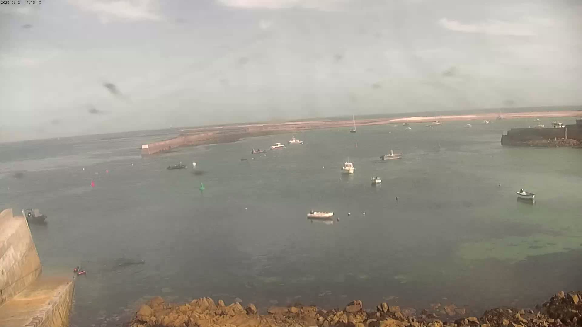 A calm, overcast day reveals a harbor filled with numerous small boats, partially enclosed by stone structures.