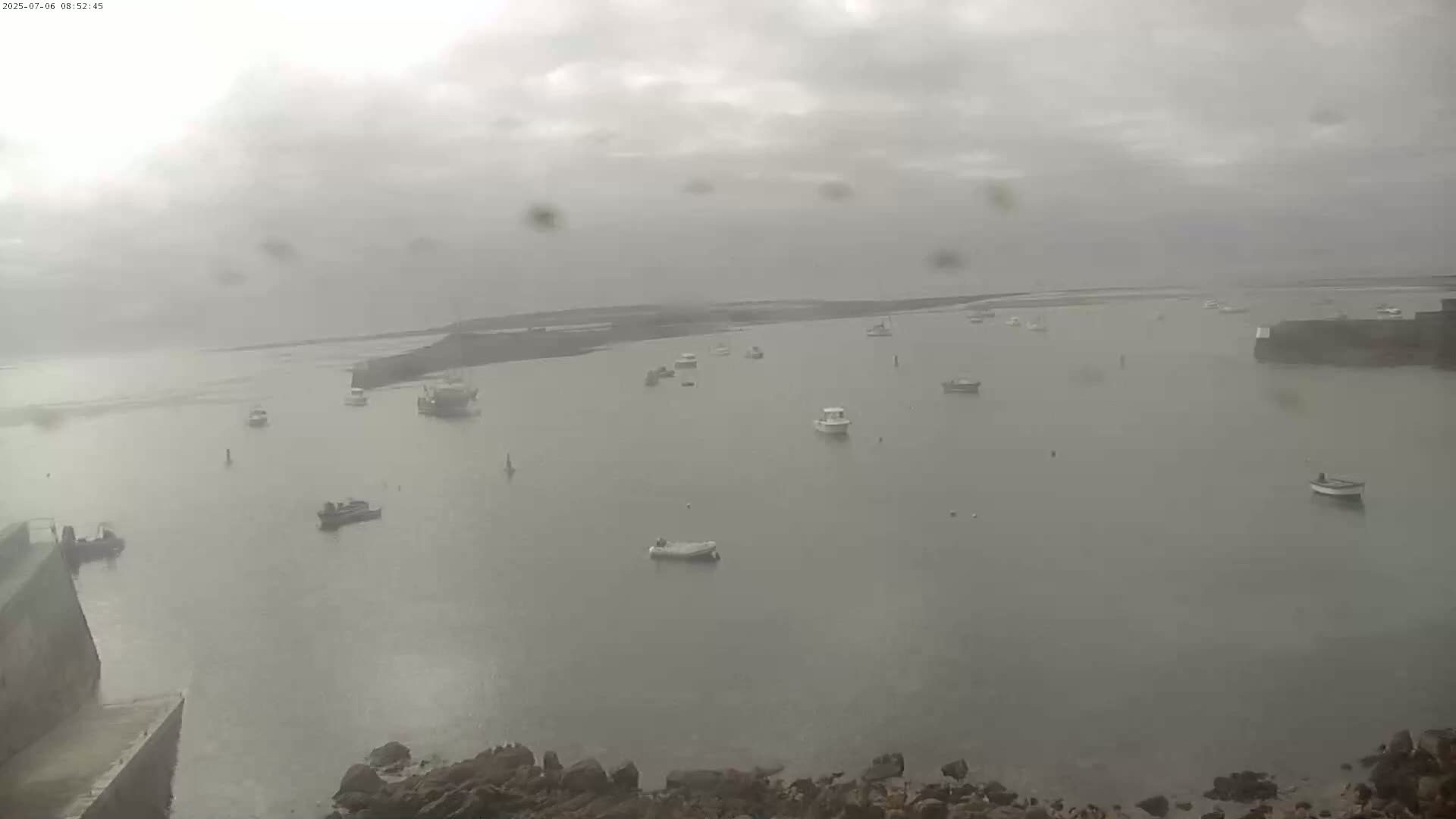 A harbor with numerous small boats is visible under an overcast, rainy sky.