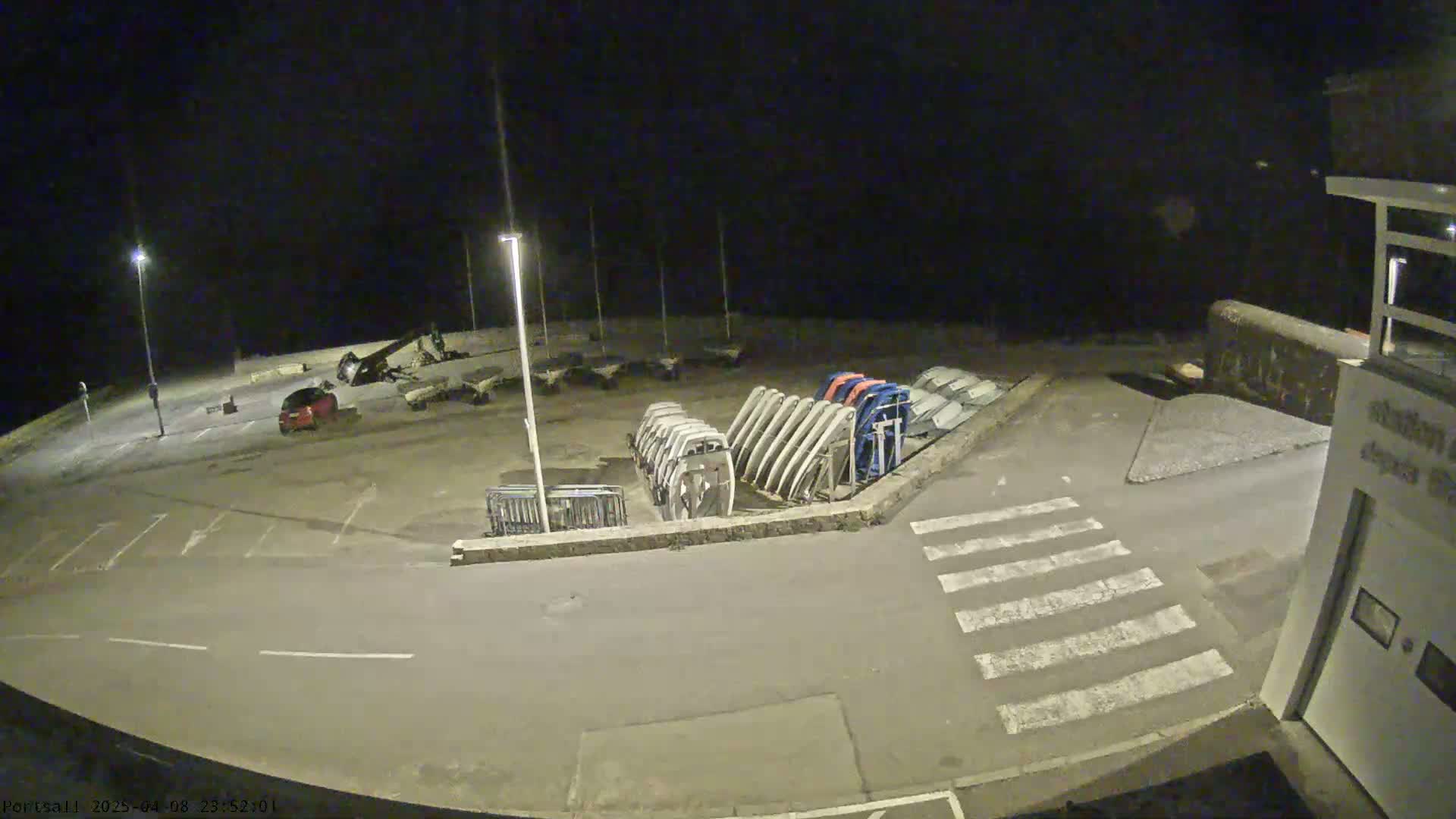 A nighttime view of an empty parking lot with several boats stored upright in a rack, next to a crosswalk.