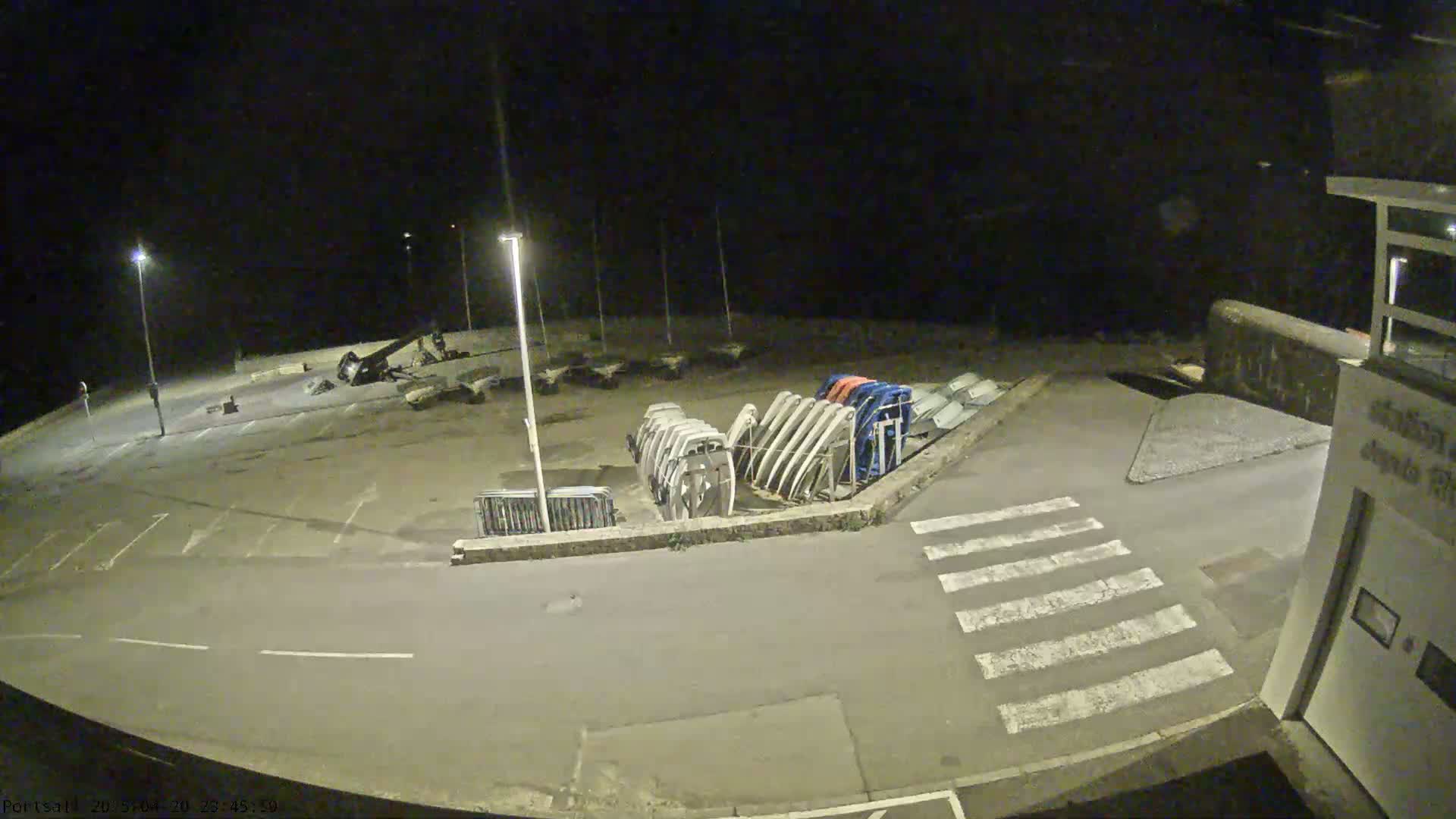 An empty nighttime parking lot with several overturned boats and a pedestrian crossing is illuminated by streetlights.