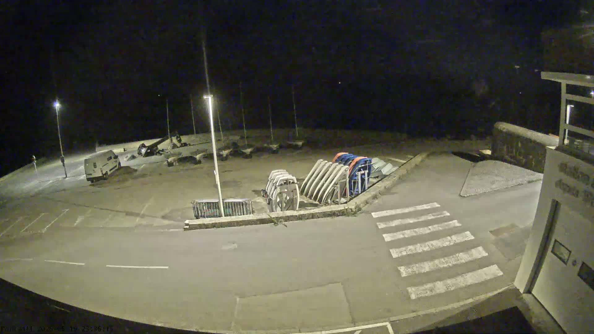 A nighttime, dimly lit parking lot contains several boats on trailers, a van, and a pedestrian crosswalk.