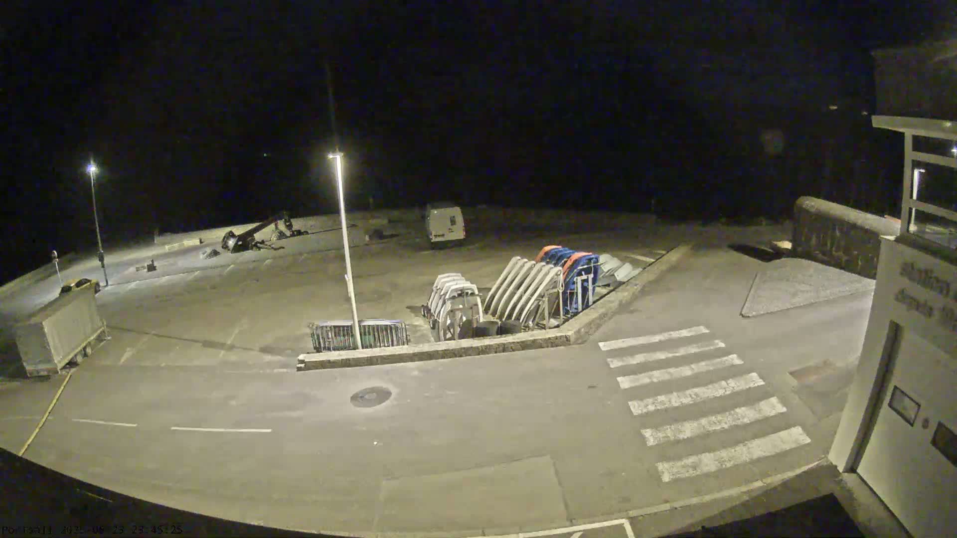 A nighttime, outdoor view of an empty parking lot with several boats on trailers, a van, and a building in the lower right corner.