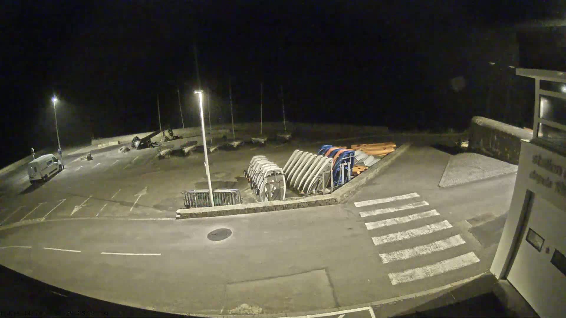 A nighttime view of an empty parking lot with several boat trailers and a single van, under dark, clear skies.