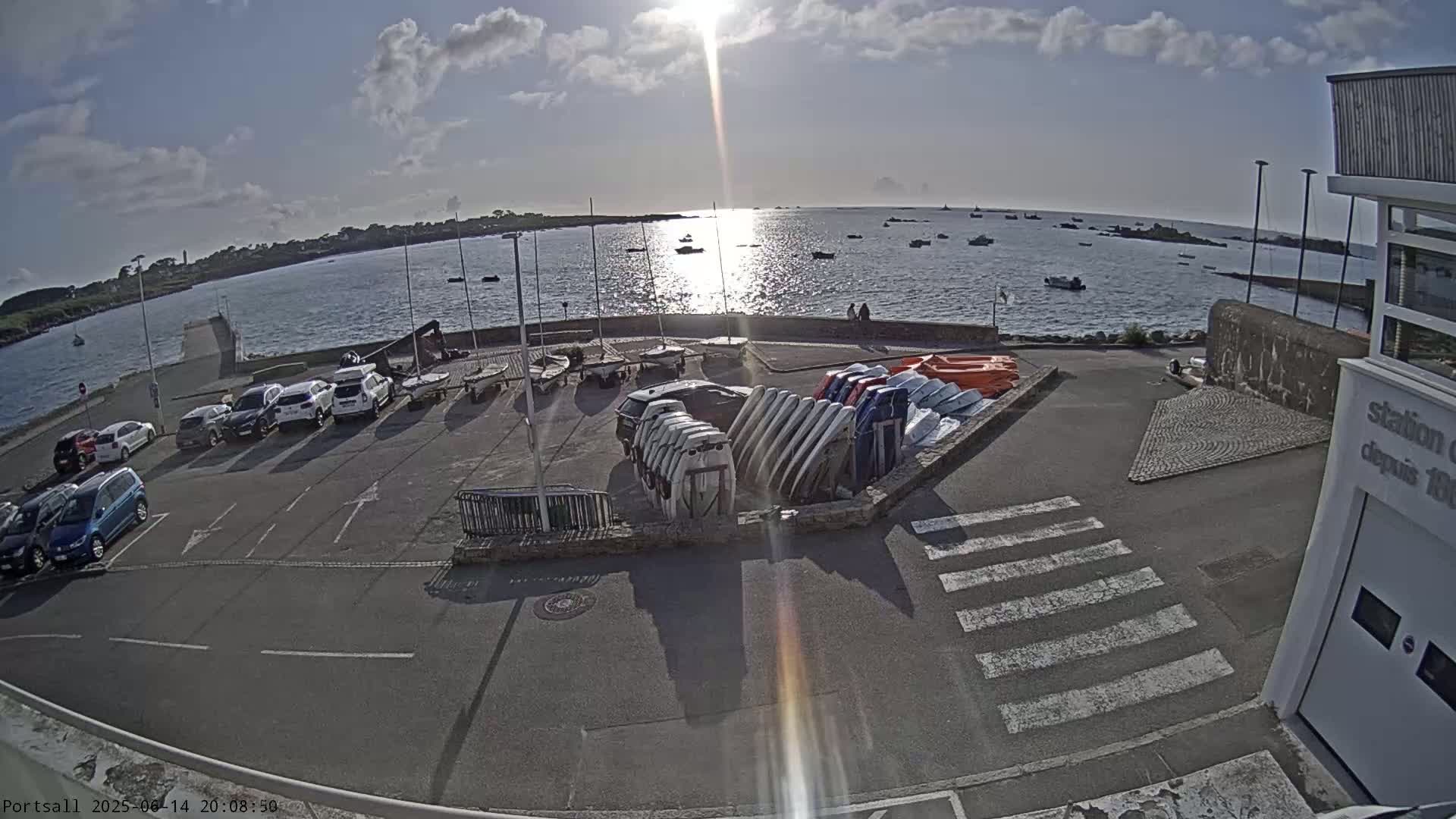 A sunny day overlooking a harbor with parked cars and numerous small boats, both in the water and stored on land.