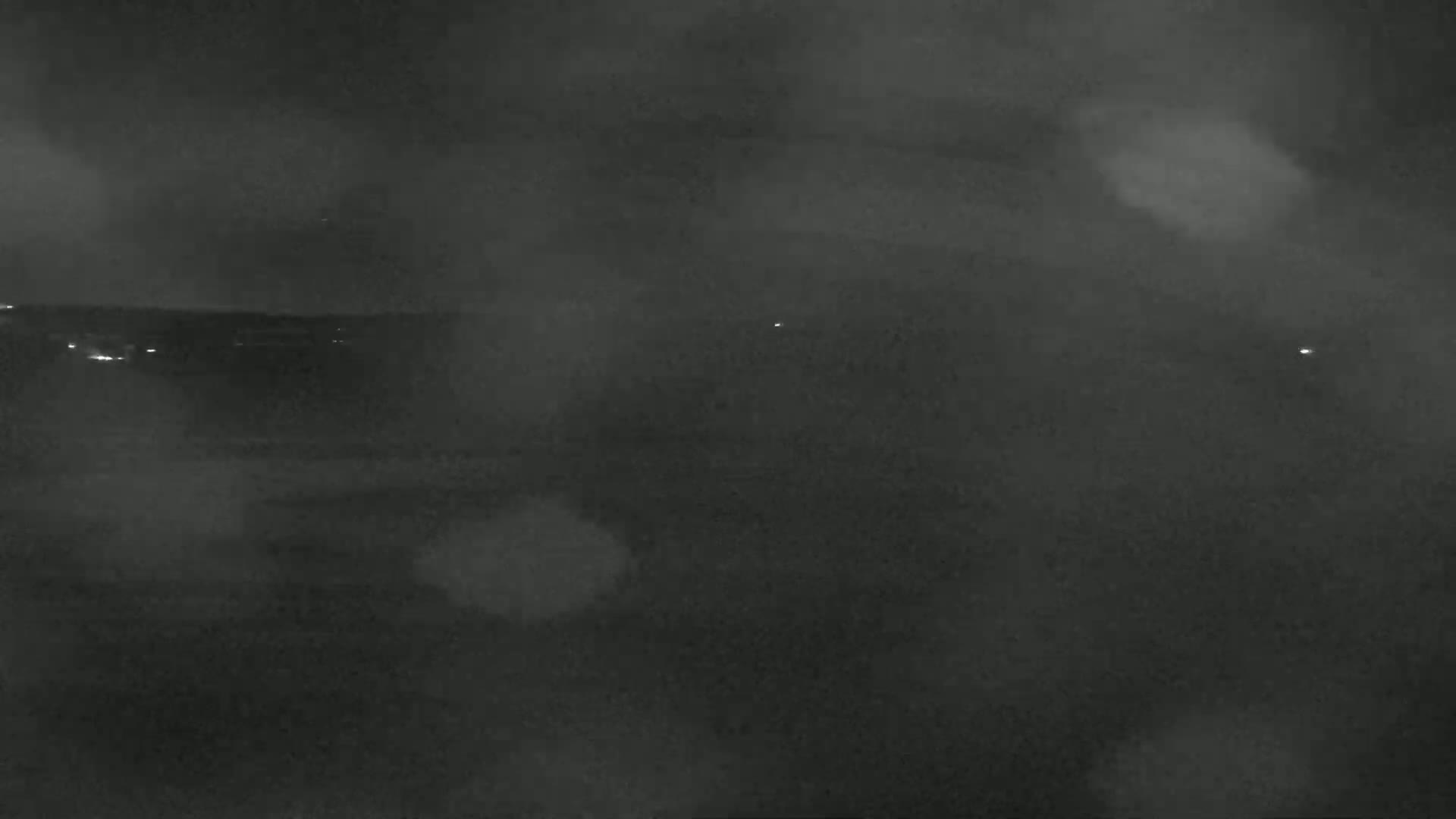 A nighttime, blurry view of a dark landscape with a few distant lights under a hazy sky.