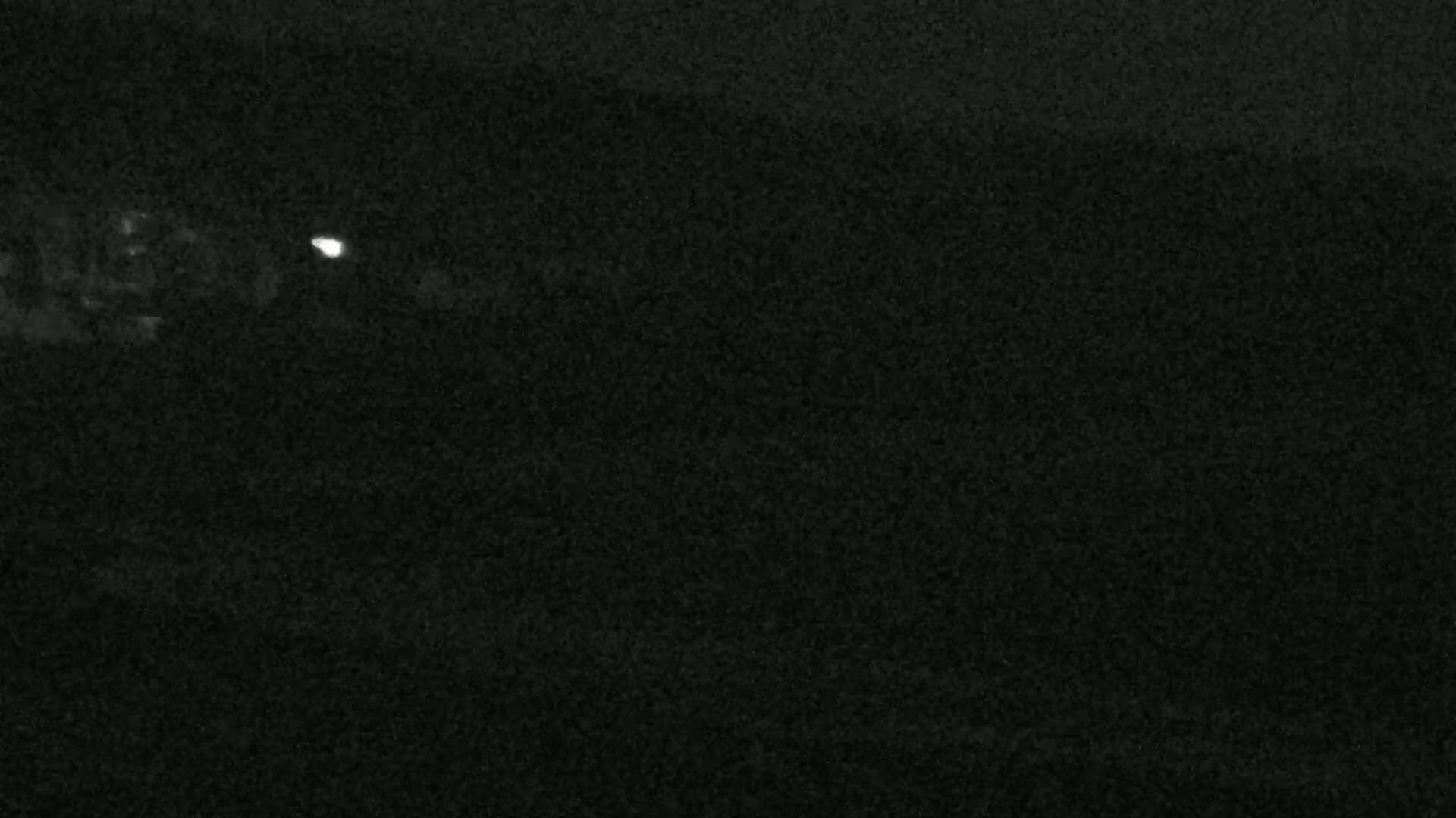 A dark, grainy image shows a faint light source in the distance at night.