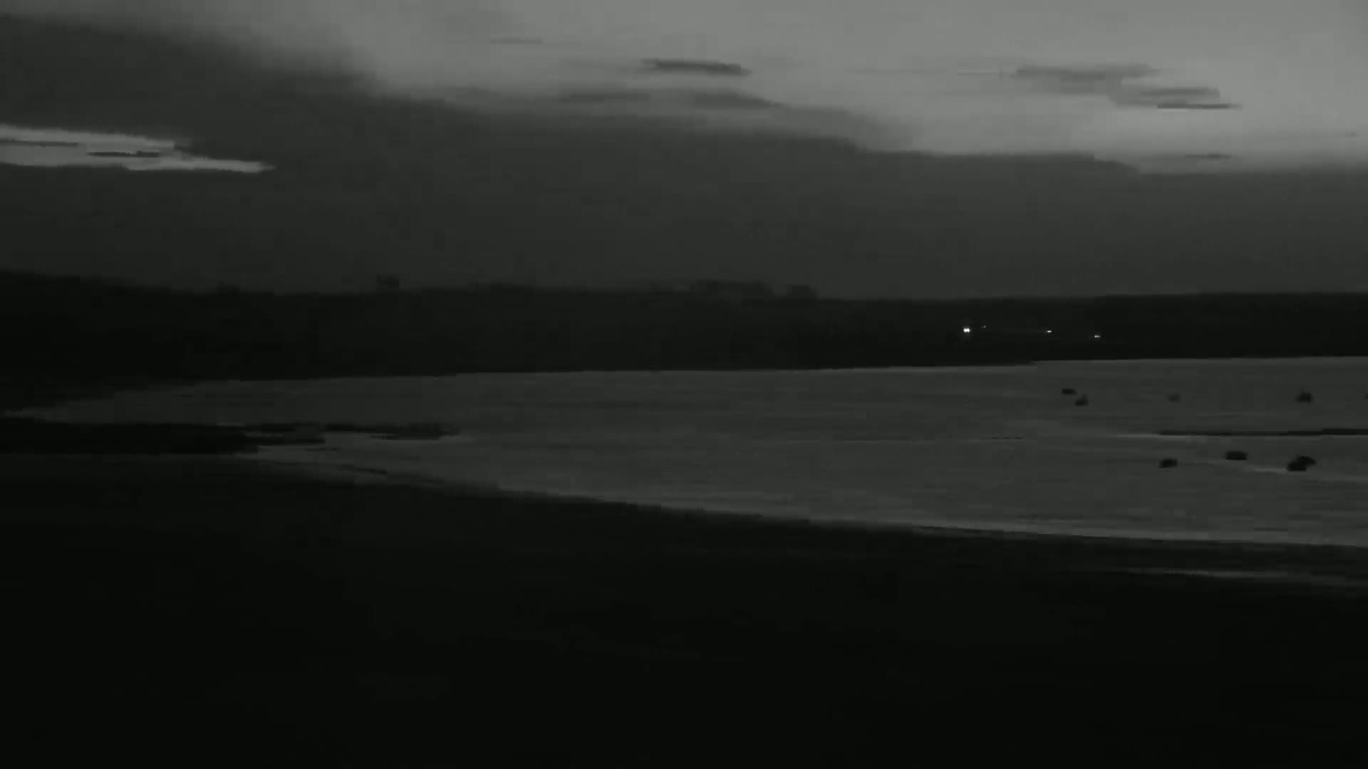 A dark, overcast sky hangs over a calm body of water, with a distant shoreline faintly visible.