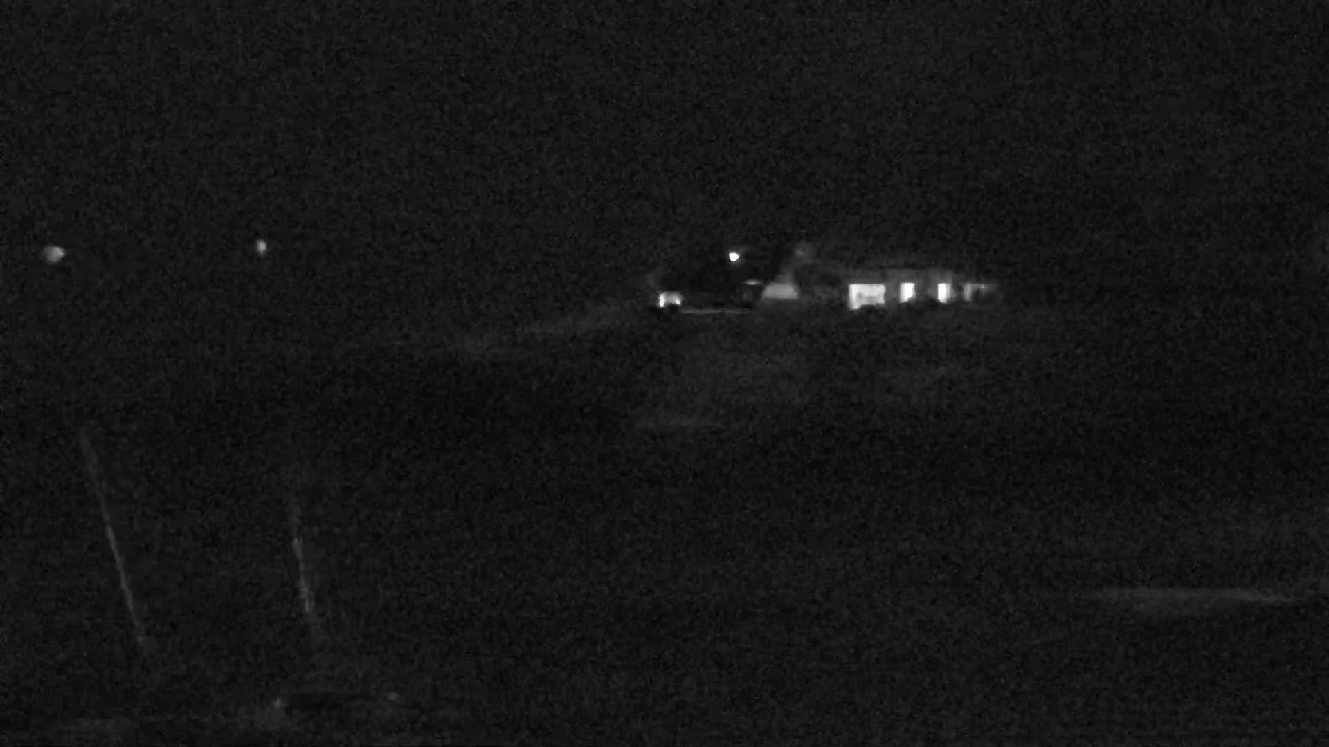 A dimly lit house is visible in the distance on a dark night.
