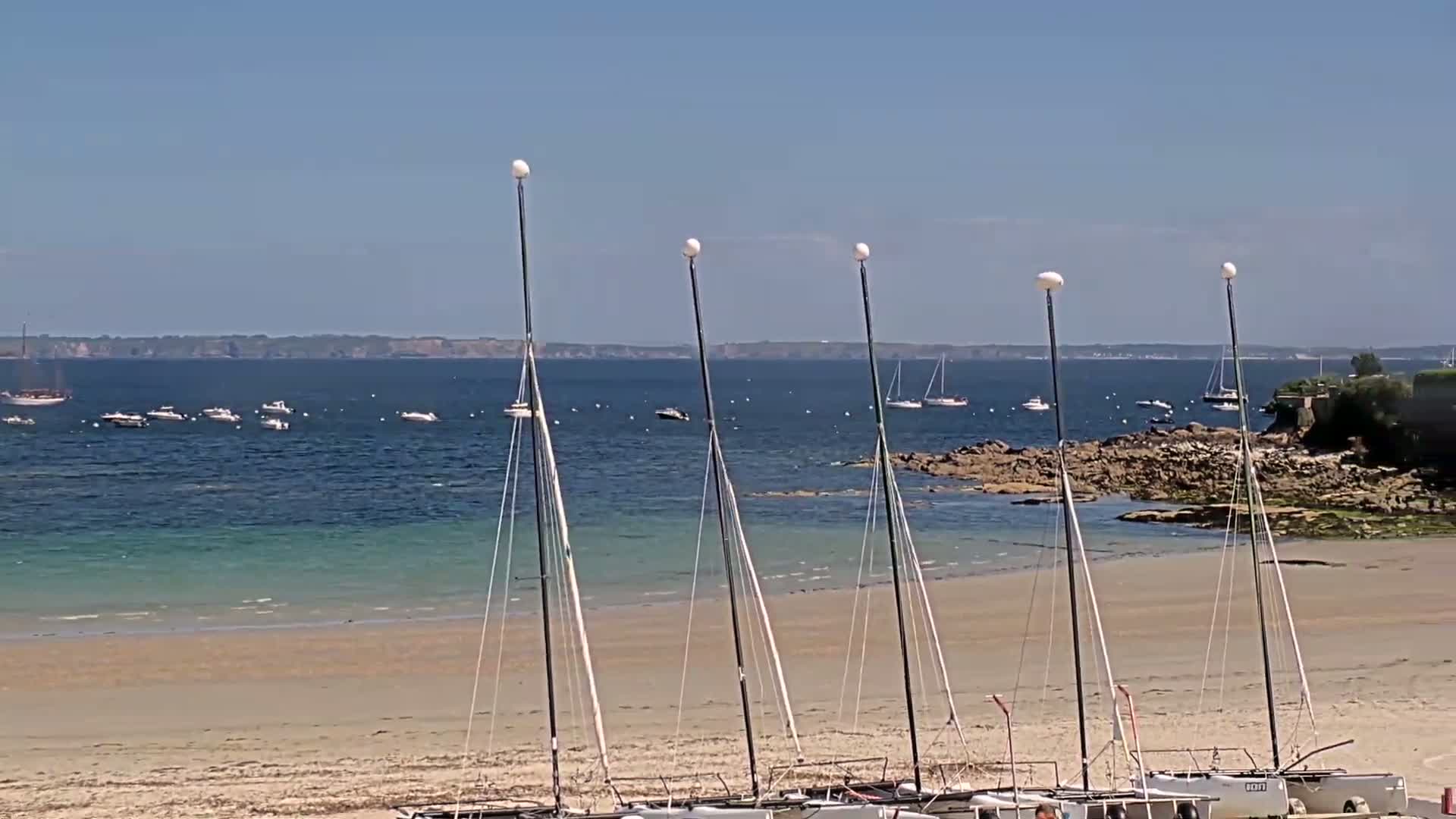 Several catamarans are beached on a sandy shore, with calm blue water and a distant coastline visible under a clear blue sky.