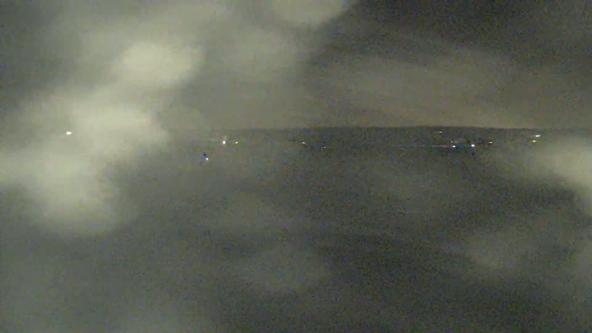 A dark, foggy nighttime scene shows a distant horizon line with faint lights.