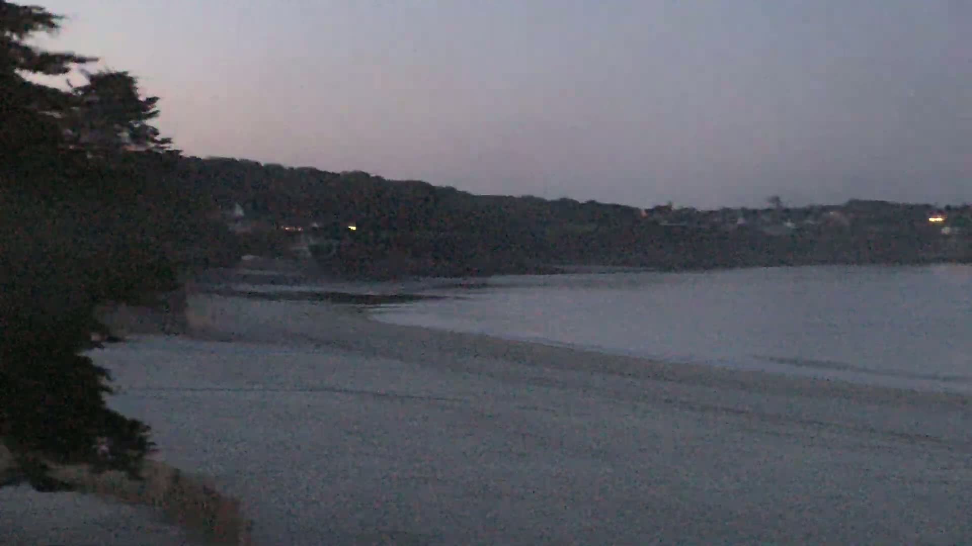 A sandy beach stretches out to a calm body of water under a dusky, twilight sky.