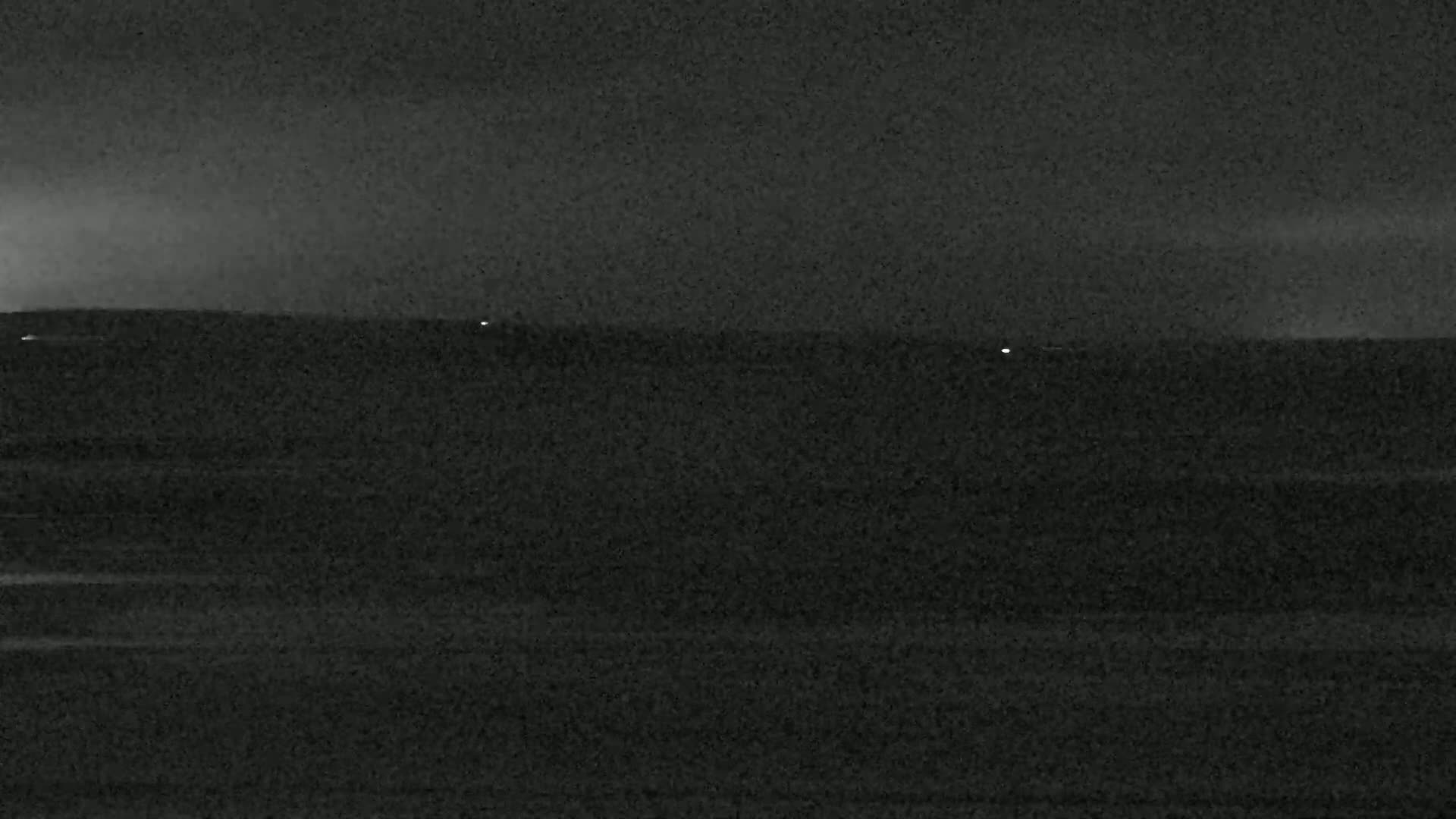 A dark, flat landscape is visible under a dark, cloudy night sky, with a few faint lights in the distance.