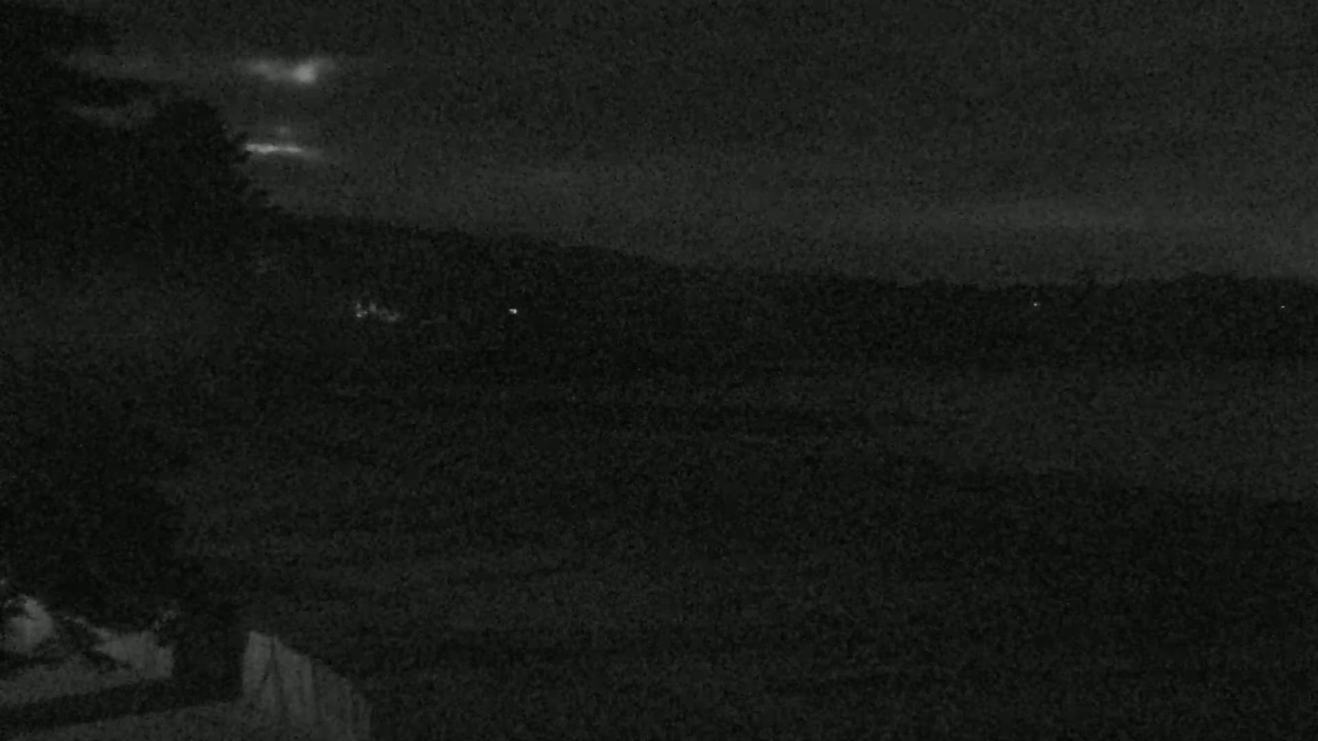 A nighttime view shows a dark landscape under a slightly cloudy sky.