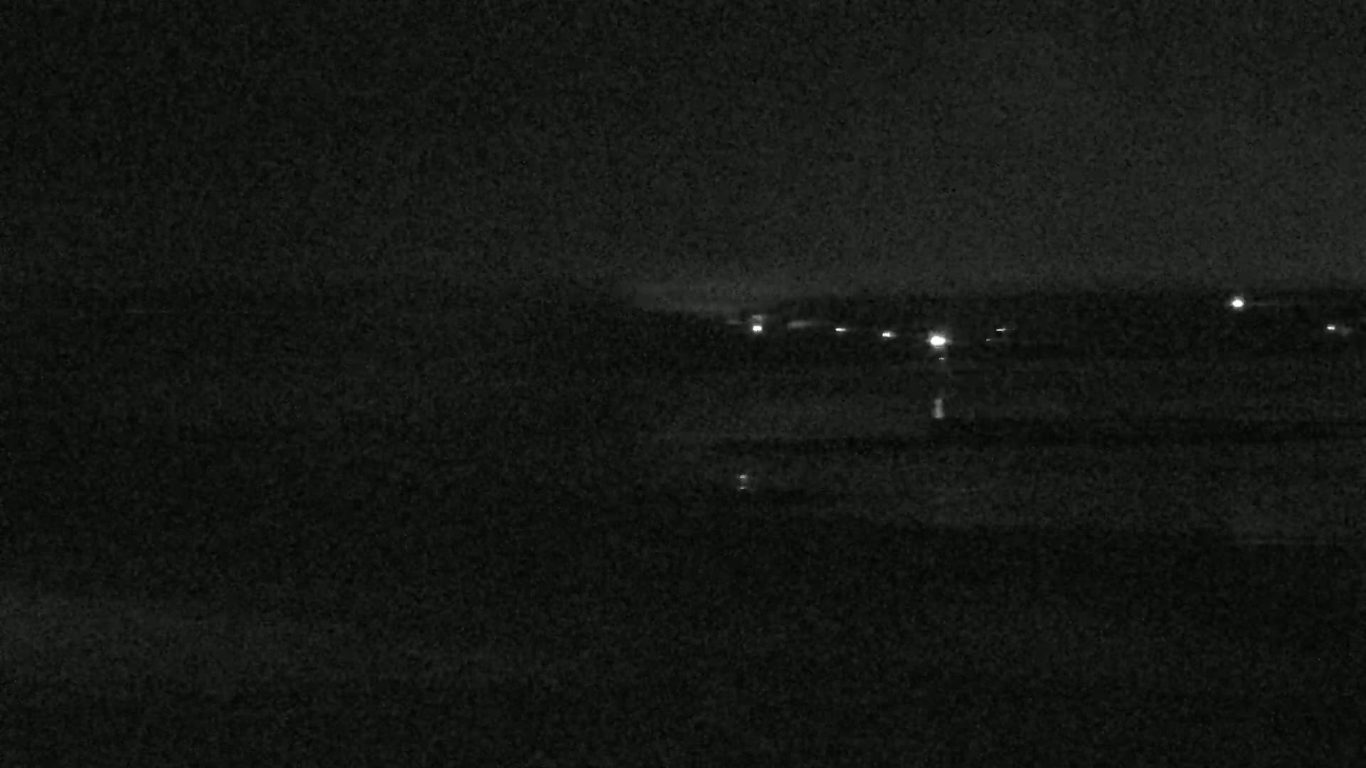 A dark, nighttime scene shows a distant line of faint lights on a horizon.