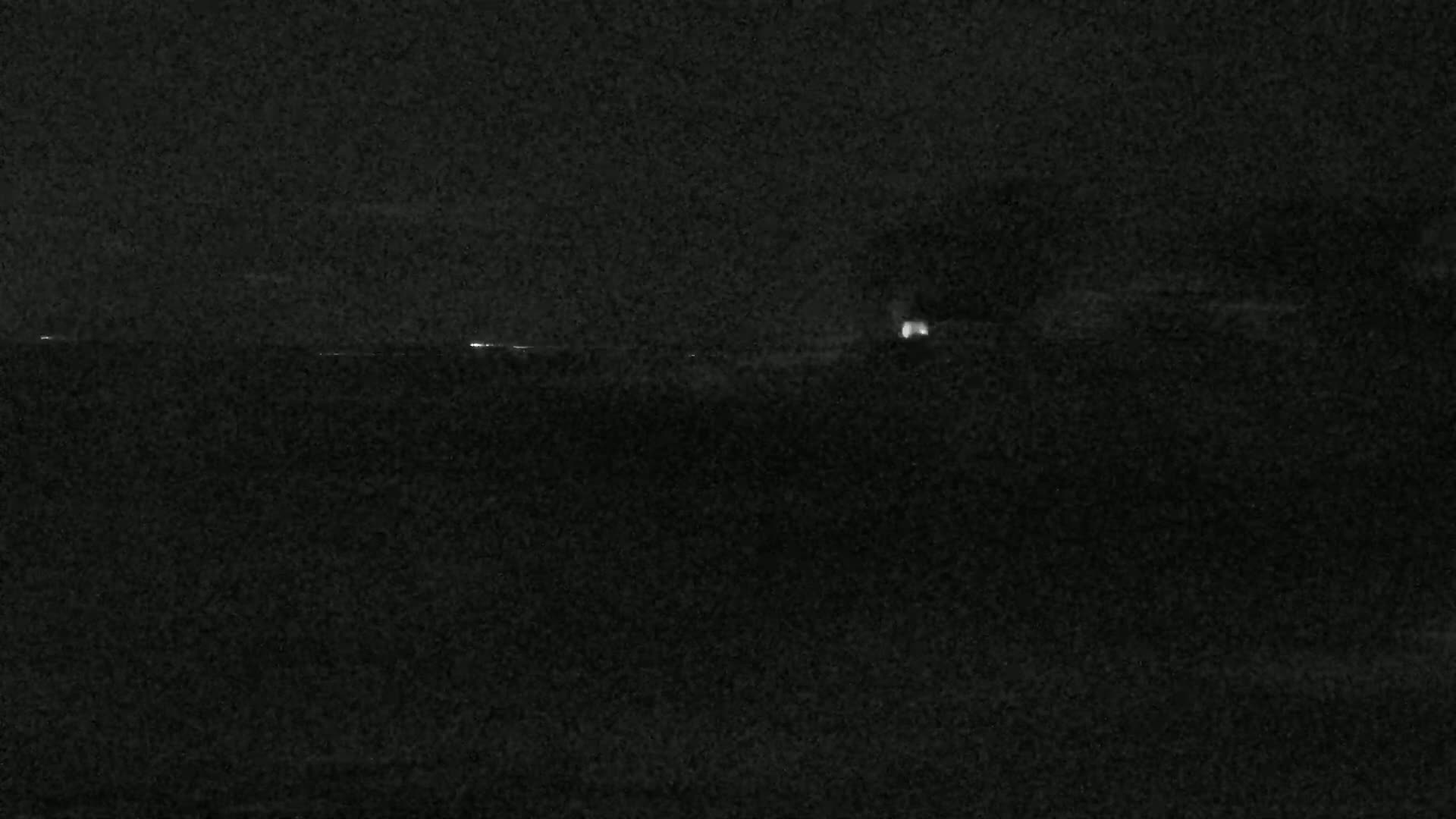 A nighttime, dark landscape with a few faint lights visible in the distance.