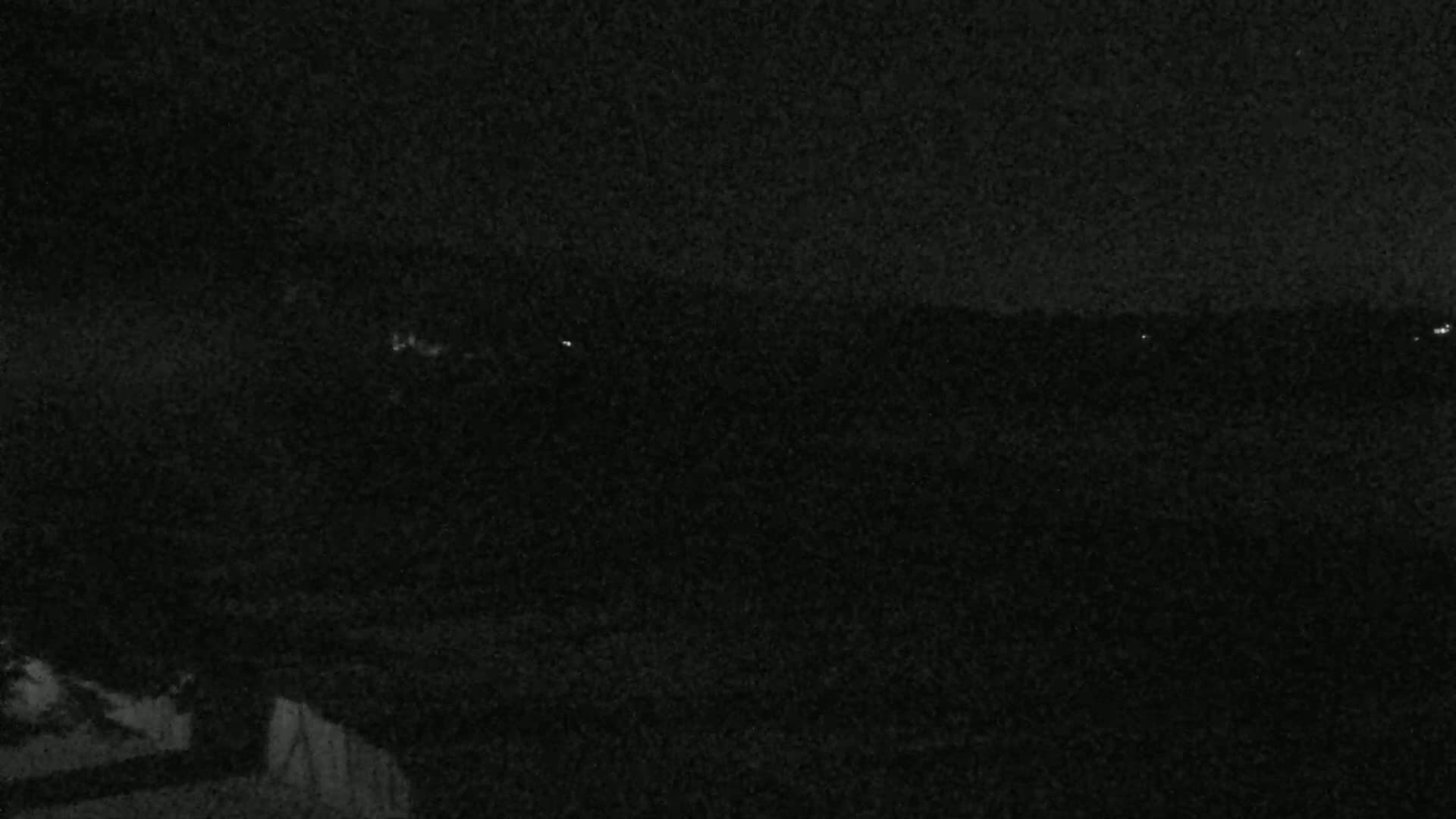 A dark, nighttime landscape shows a distant horizon line with faint lights, possibly from a town or city.