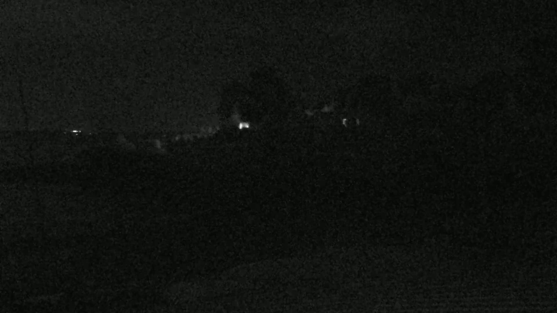 A dark, nighttime landscape shows a few faint lights in the distance.