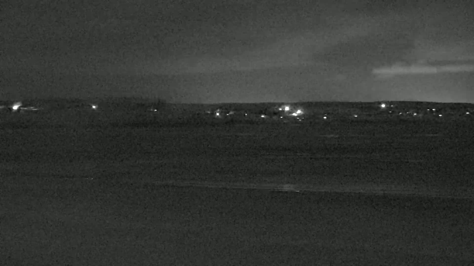 A nighttime long shot shows a dark landscape with a line of distant lights under a mostly clear sky.