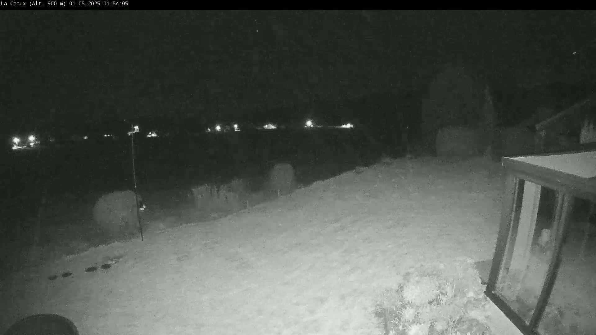 A snow-covered backyard at night is illuminated by distant lights, with a section of a building visible in the lower right corner.