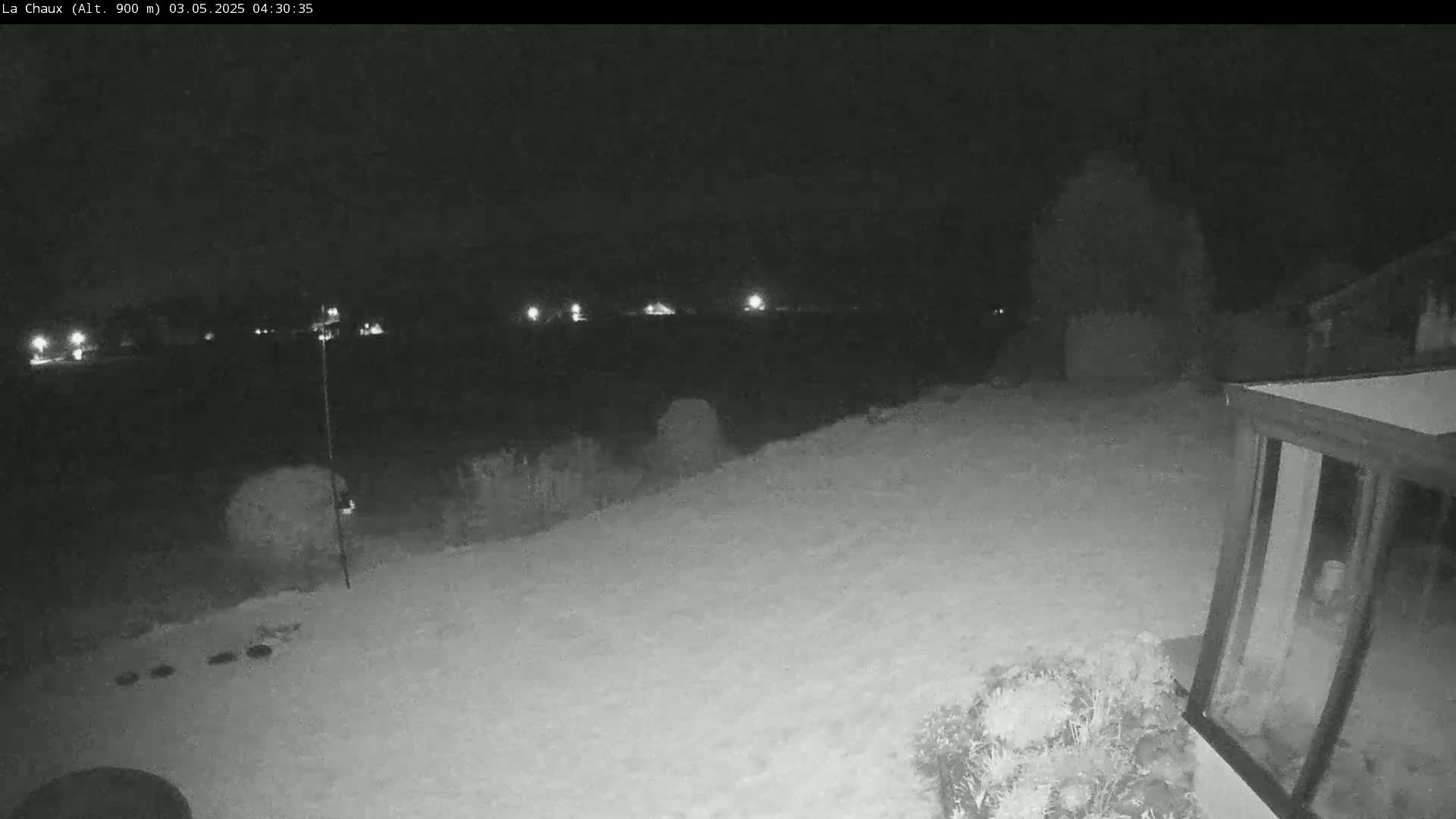 A snow-covered backyard at night is illuminated by distant lights, with a building visible in the lower right corner.