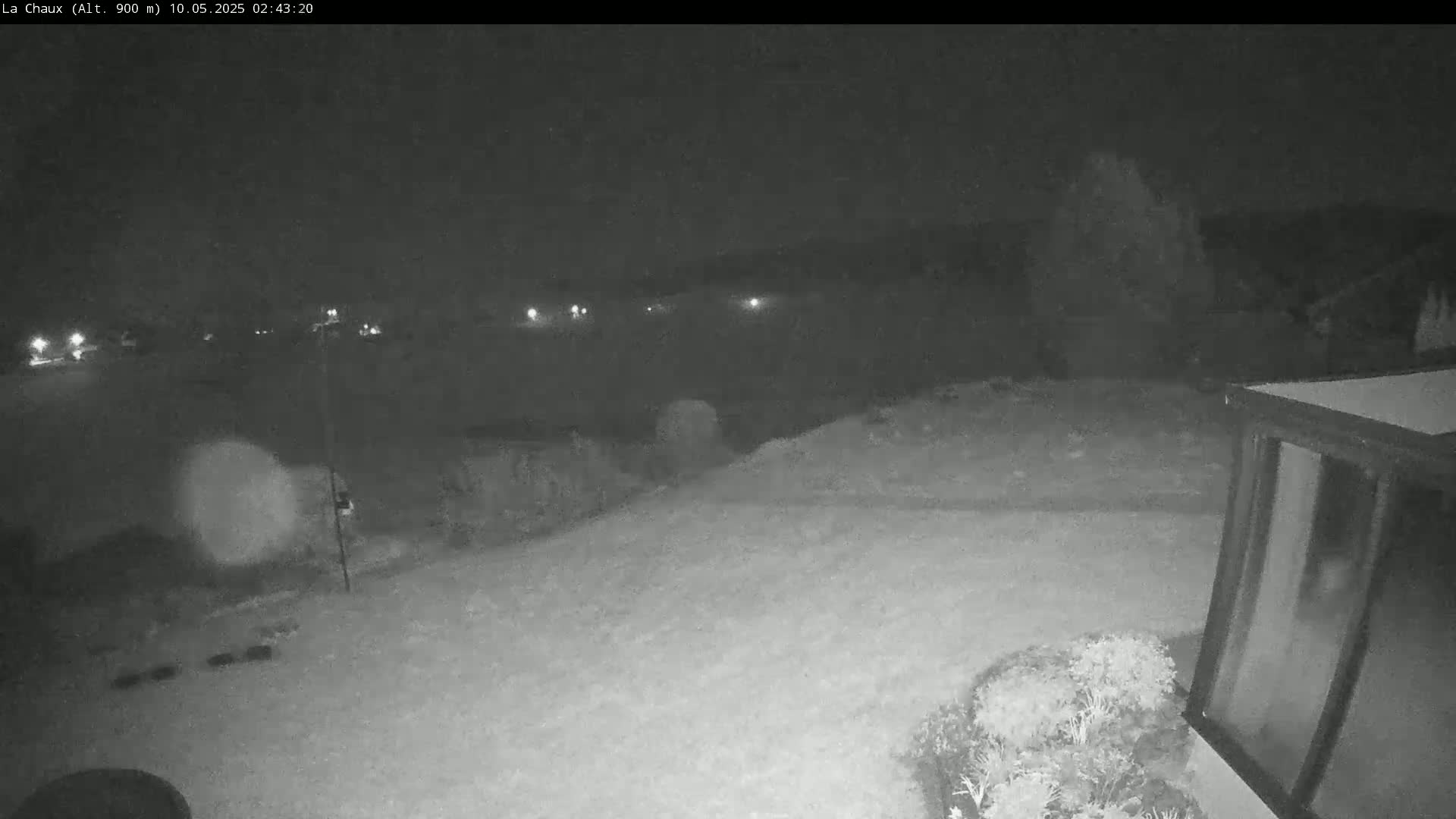 A nighttime, snow-covered landscape is visible from a security camera, showing a portion of a building and distant lights.