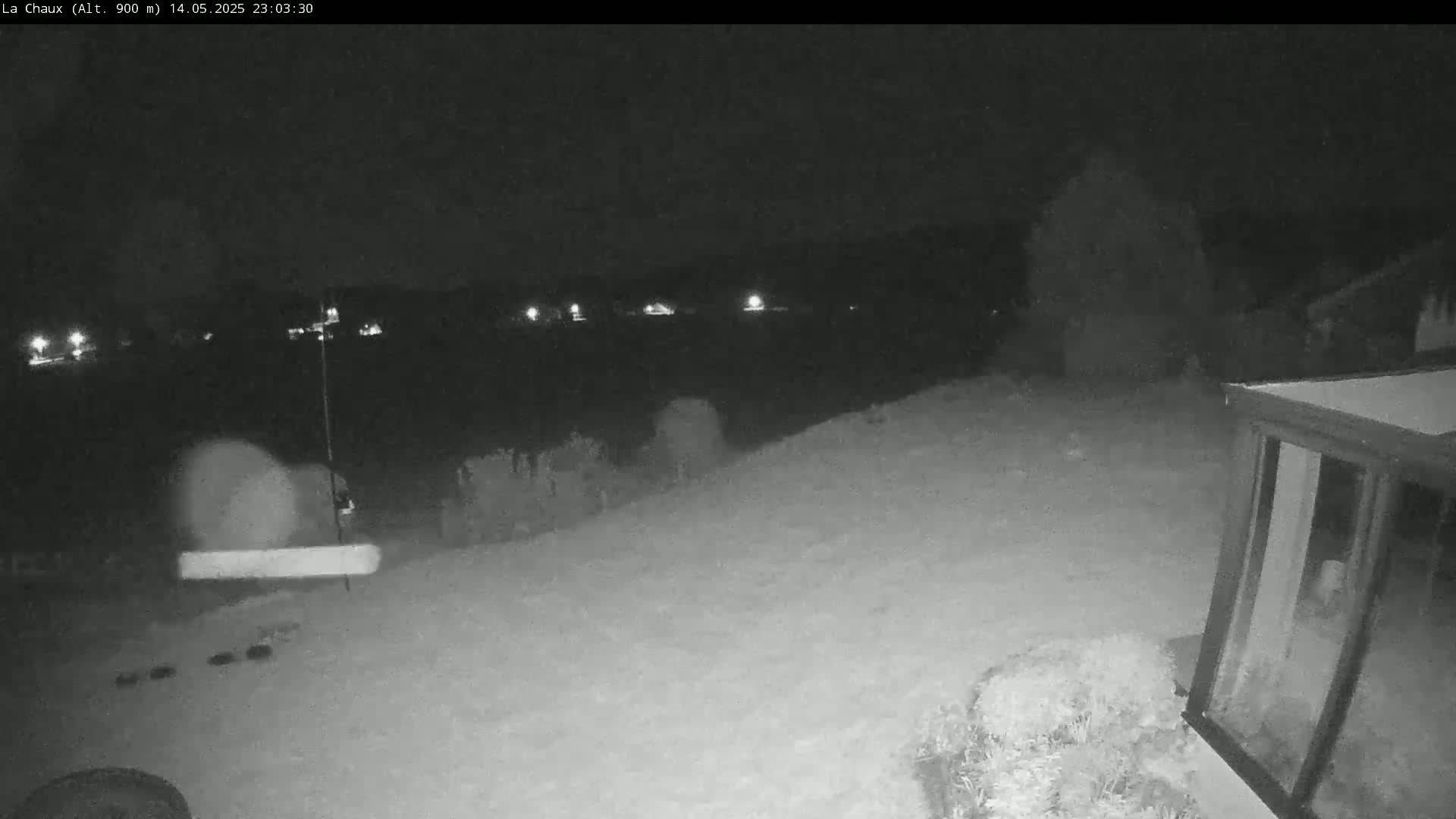 A snow-covered backyard at night is illuminated by distant lights, with a structure visible in the lower right corner.
