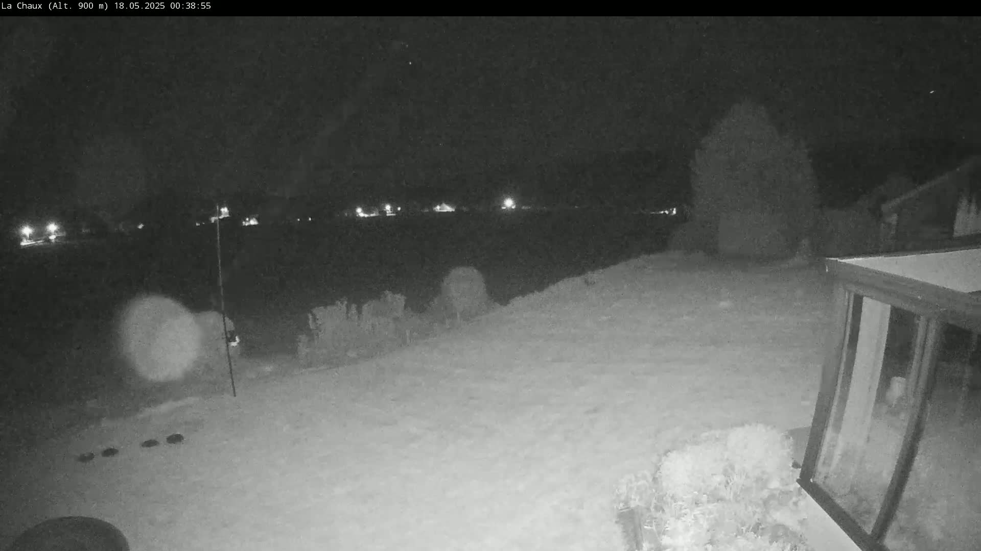 A snow-covered backyard at night is illuminated by distant lights, with a structure visible in the bottom right corner.
