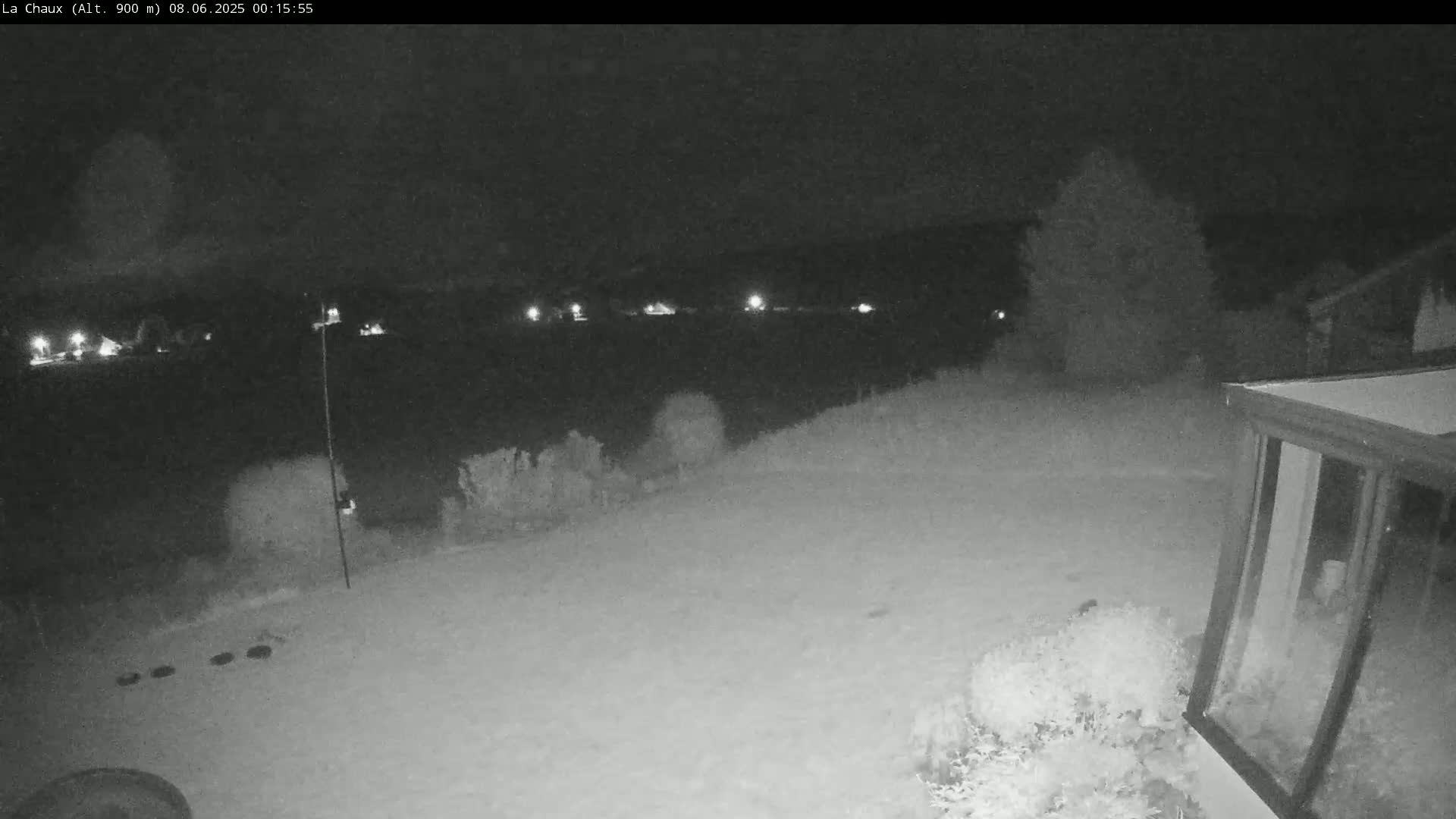 A snow-covered backyard at night is illuminated by distant lights, with a portion of a sunroom visible in the bottom right corner.