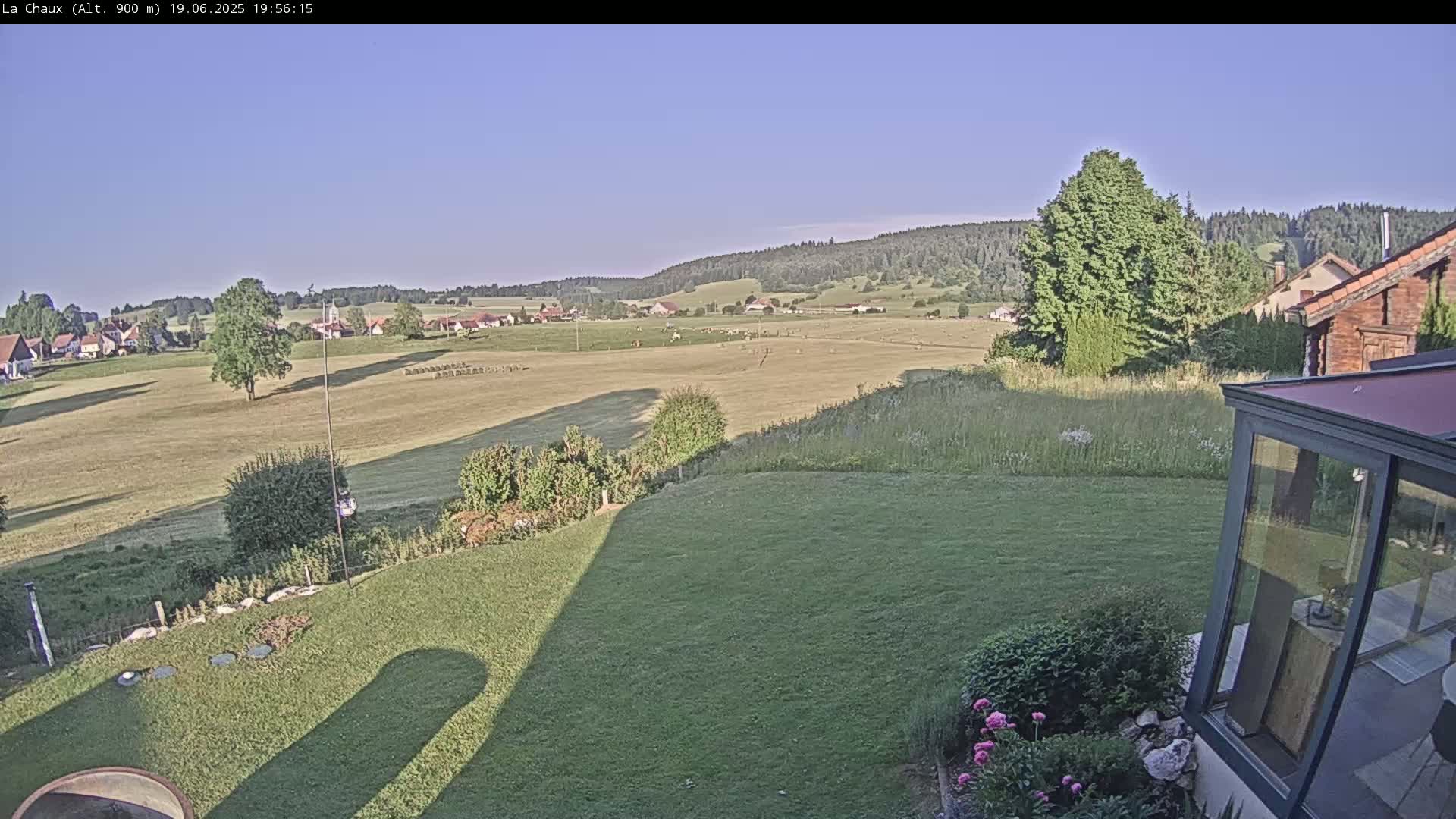 A grassy field with a village and distant hills in the background, under a clear sky.