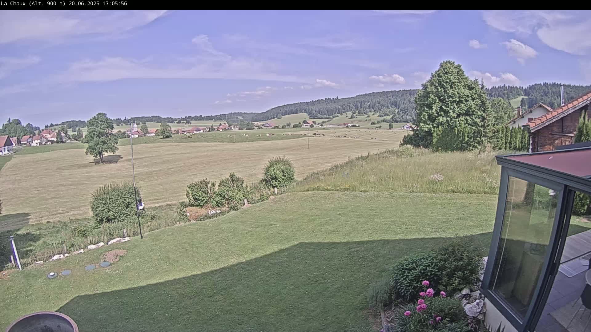 A sunny day reveals a sprawling green lawn, leading to a distant village nestled in a valley surrounded by verdant hills and forests.