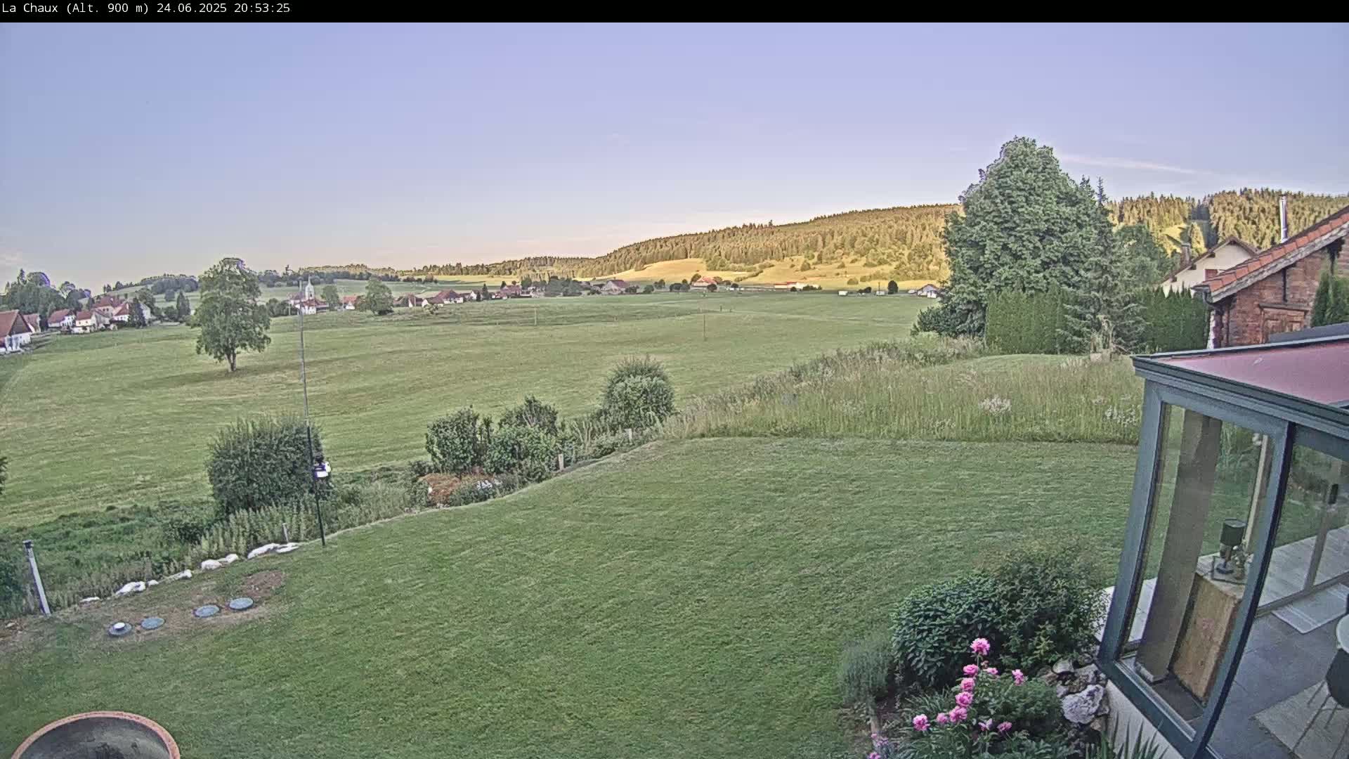 A verdant lawn slopes down to a wide expanse of green fields and distant hills under a clear, twilight sky.