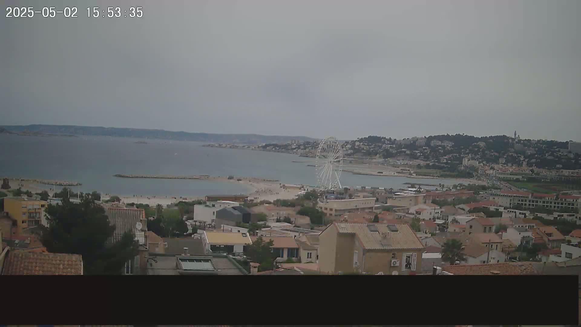 A coastal town with a Ferris wheel is visible on a partly cloudy day, overlooking a calm bay.