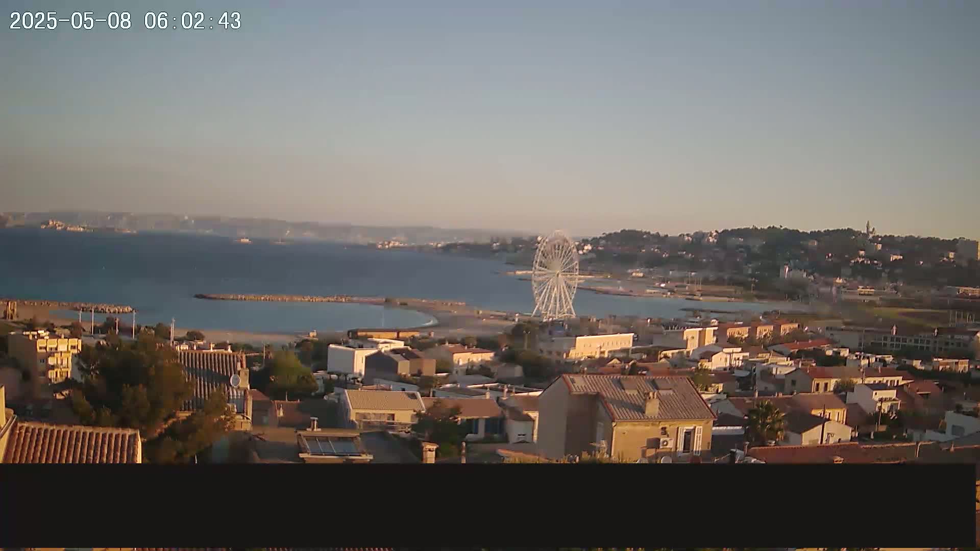 A coastal town with a Ferris wheel on the beach is visible at sunrise under a clear sky.
