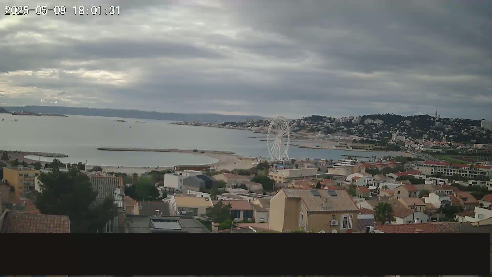 A coastal town with a Ferris wheel is visible under a cloudy sky, overlooking a calm bay.