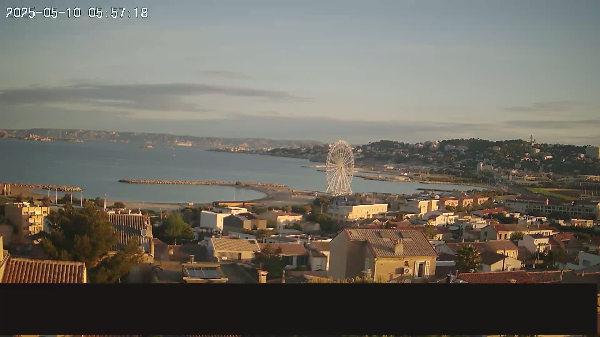 A coastal town with a Ferris wheel is visible on a calm, slightly cloudy morning.